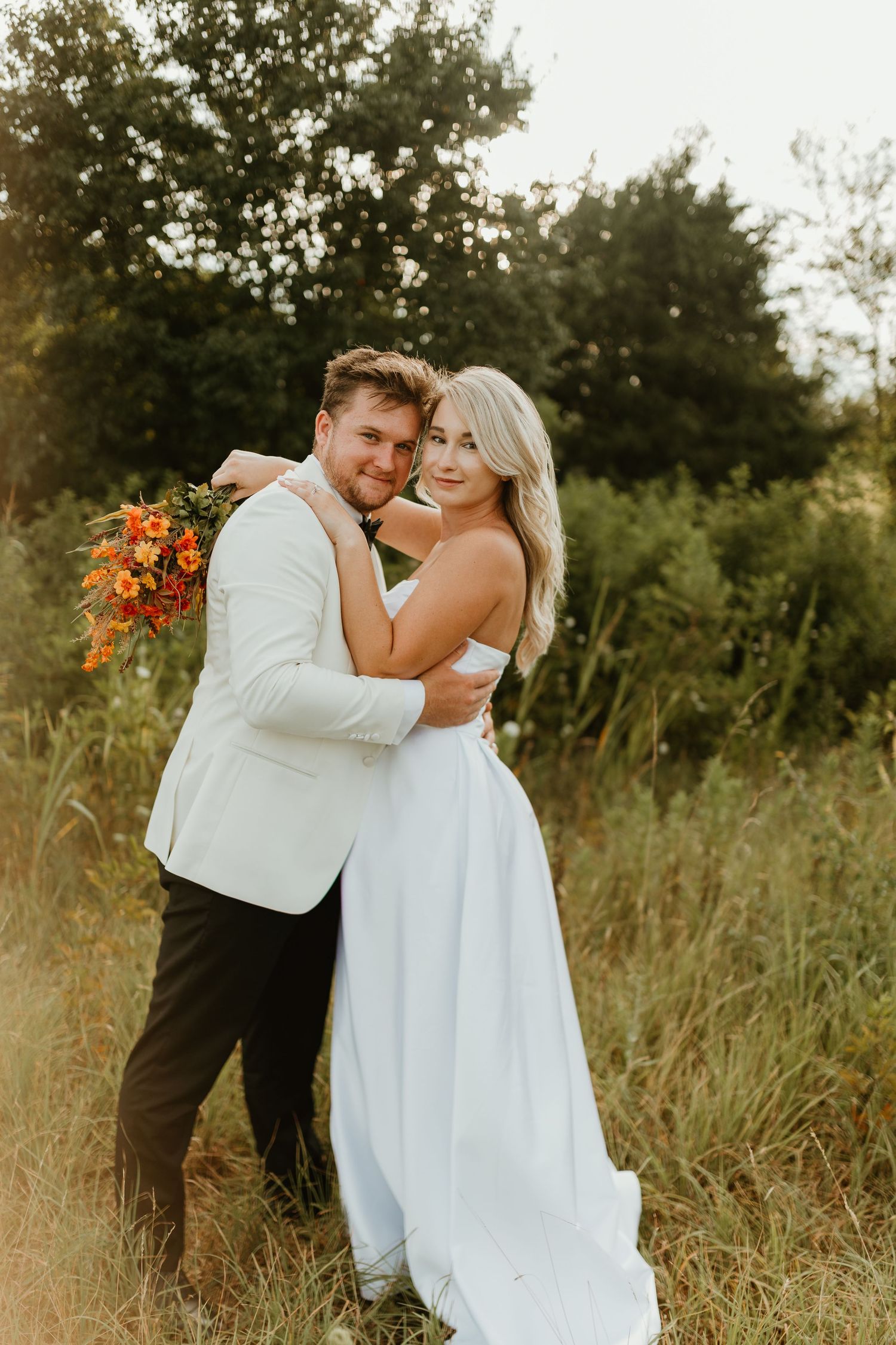 A couple shares intimate moments in a field with tall grass and wildflowers during golden hour.