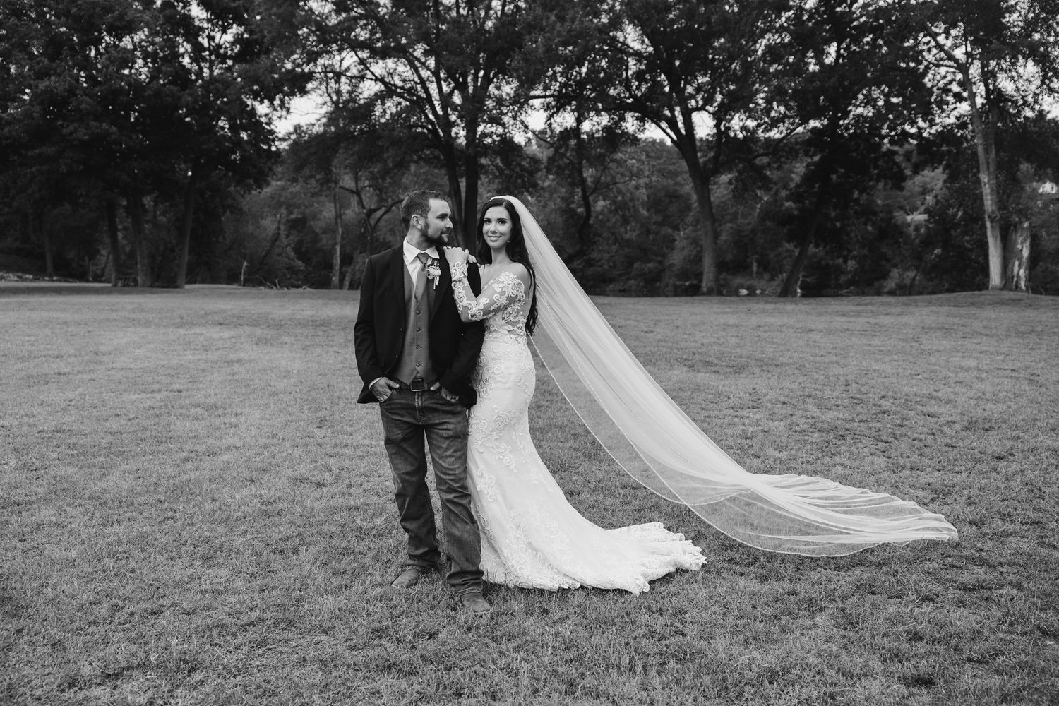 A couple in wedding attire walks together through a scenic outdoor field during their special day.