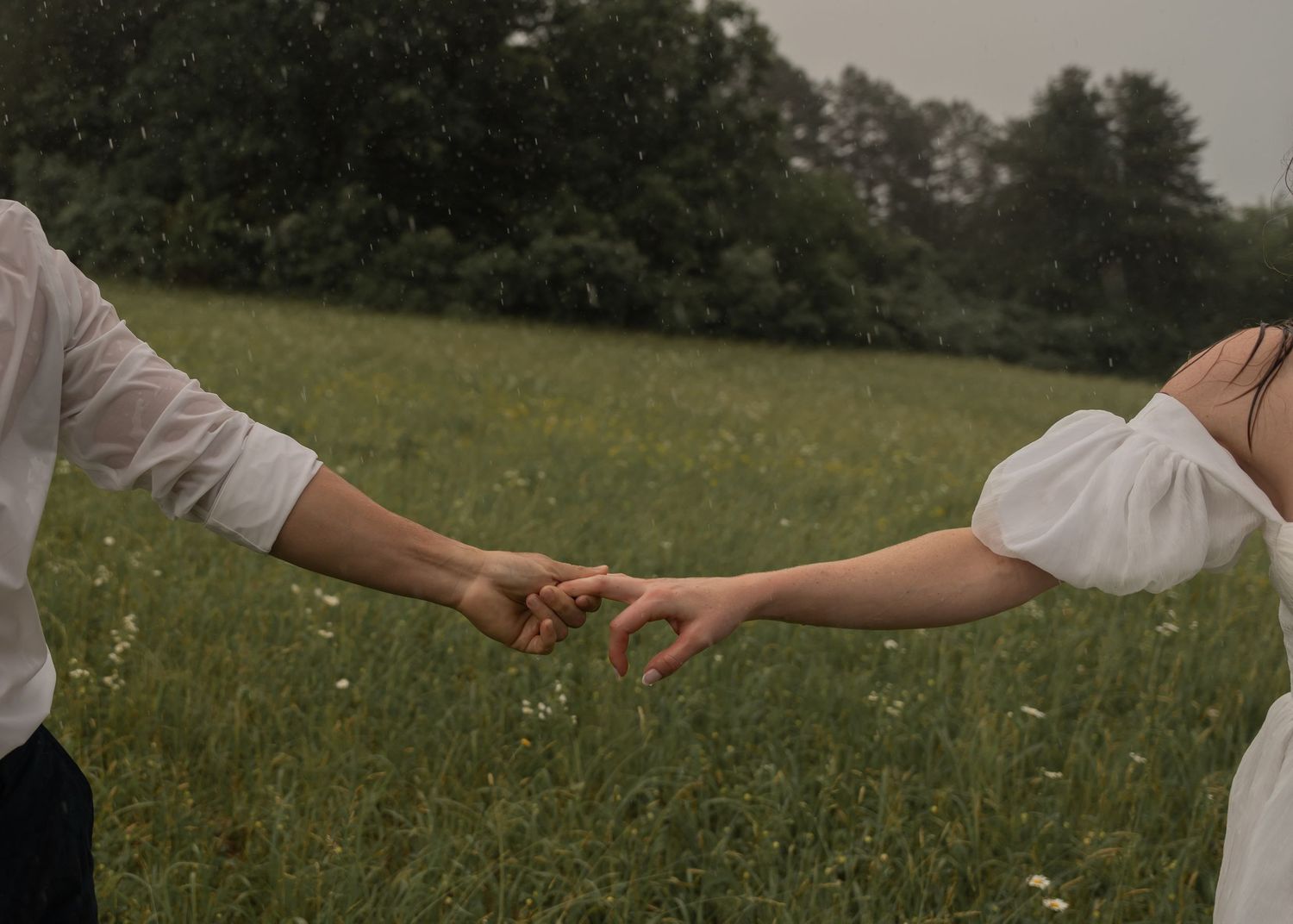 Two people reaching out to hold hands in a green meadow during a warm summer day.