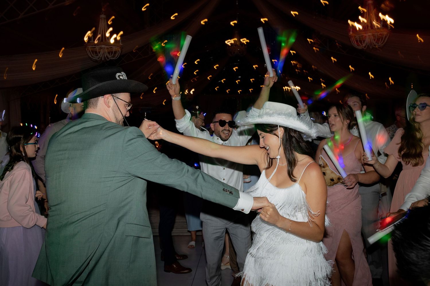 People dancing and celebrating at a lively wedding reception with colorful lights and festive atmosphere.