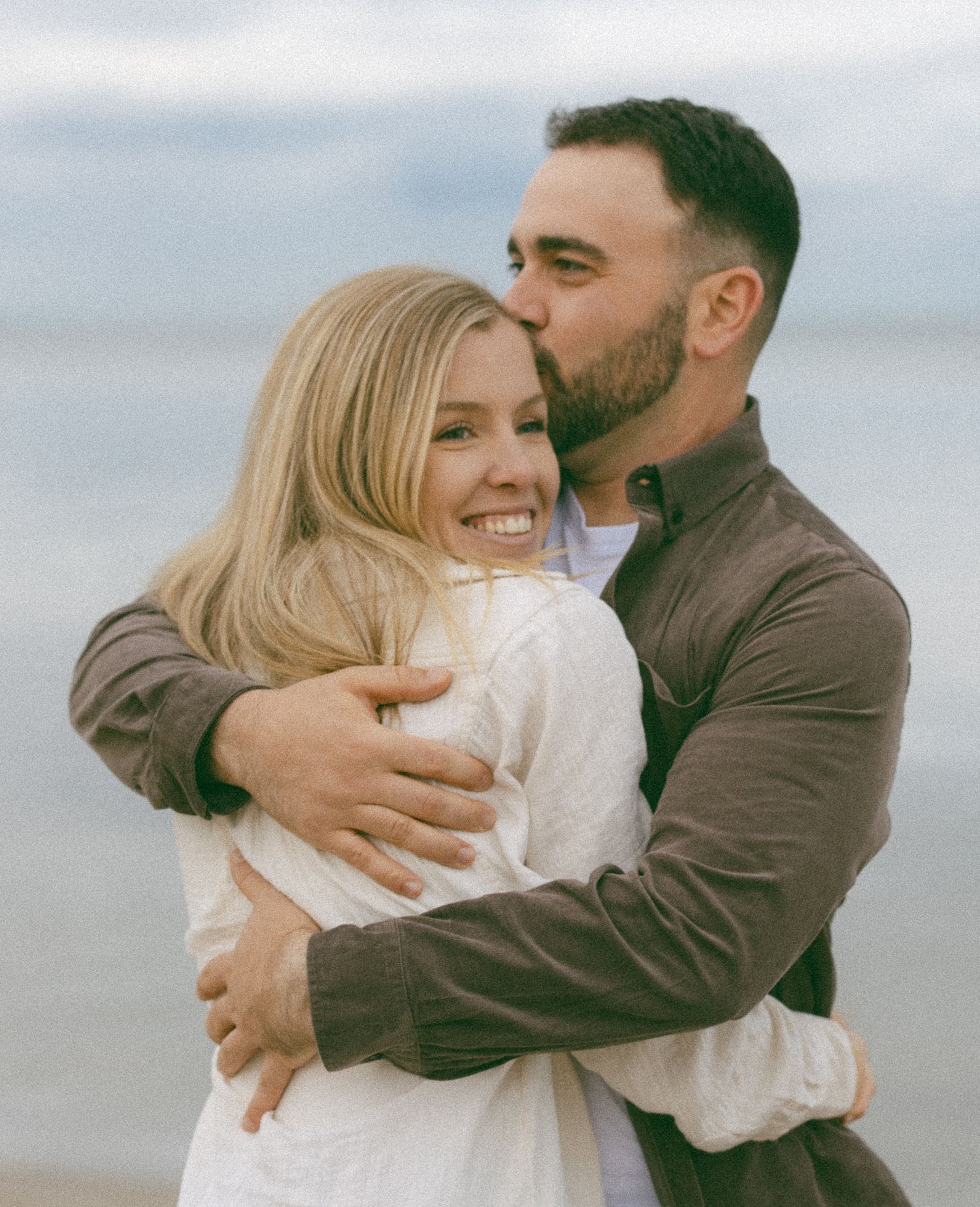 A couple shares intimate embraces on a cloudy beach in a series of romantic photographs.