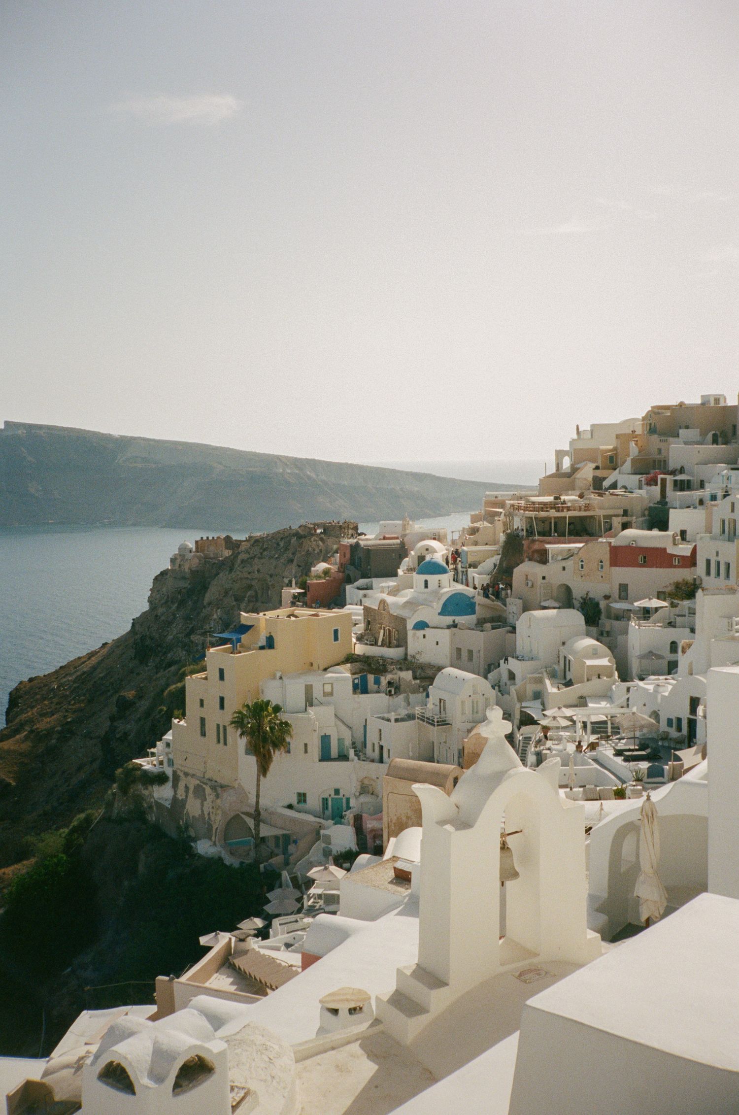 A panoramic view of white-washed buildings cascading down the cliffs of Santorini, Greece with the Aegean Sea in the background.