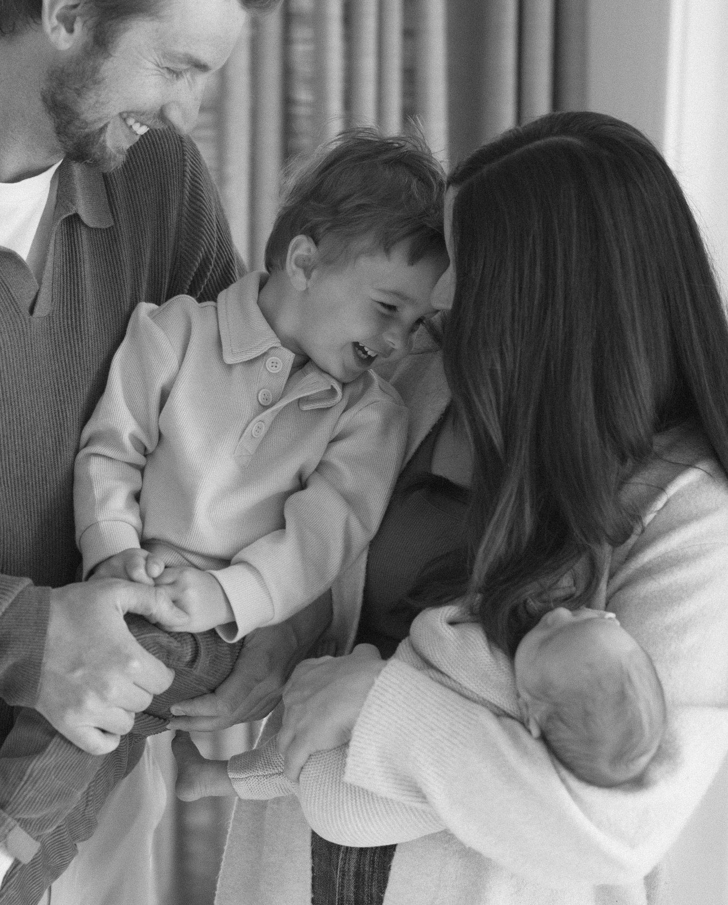 A black and white candid family moment showing parents sharing a joyful laugh with their young child.