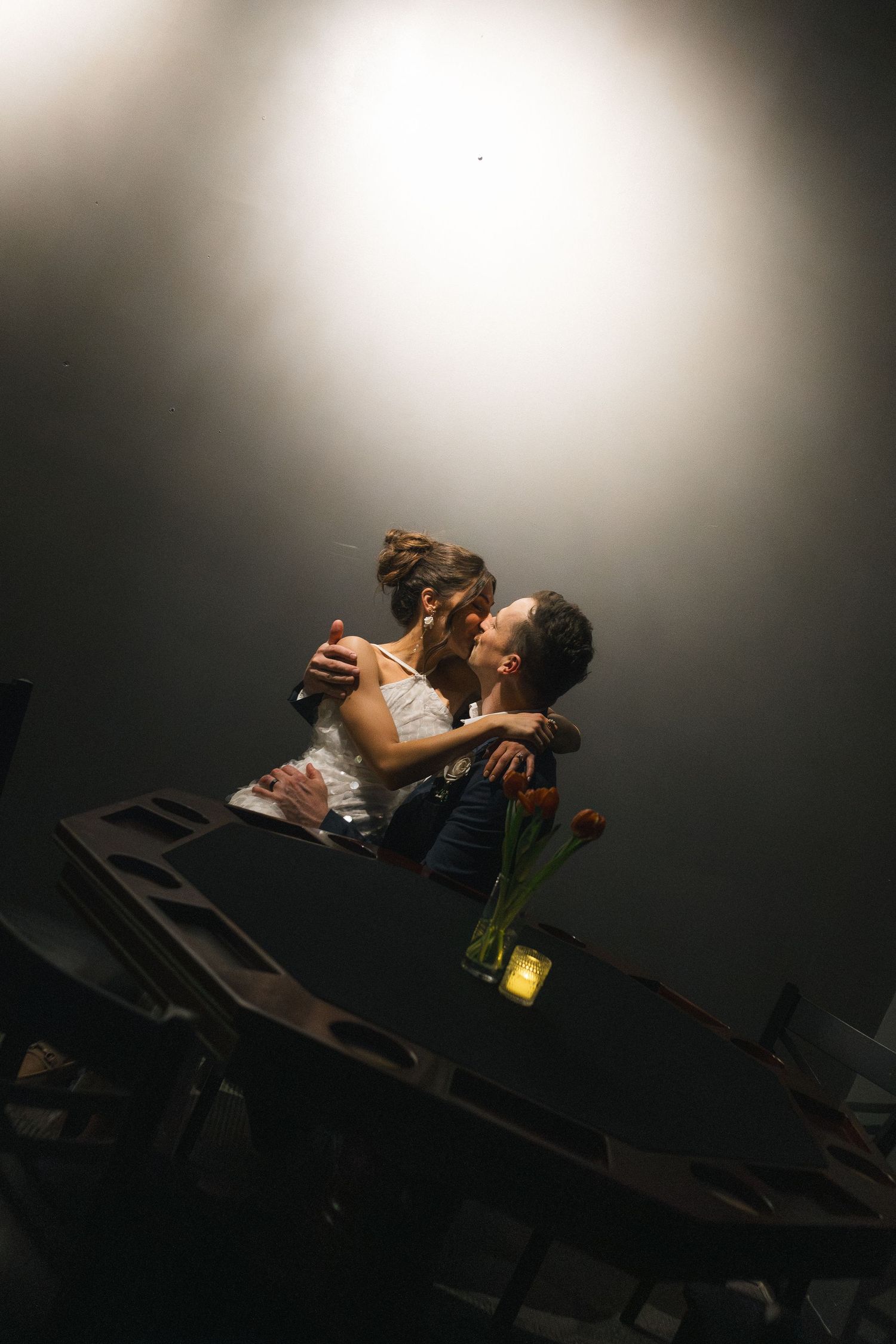 Couple sharing a romantic embrace at a candlelit dinner table with tulips under a warm spotlight.