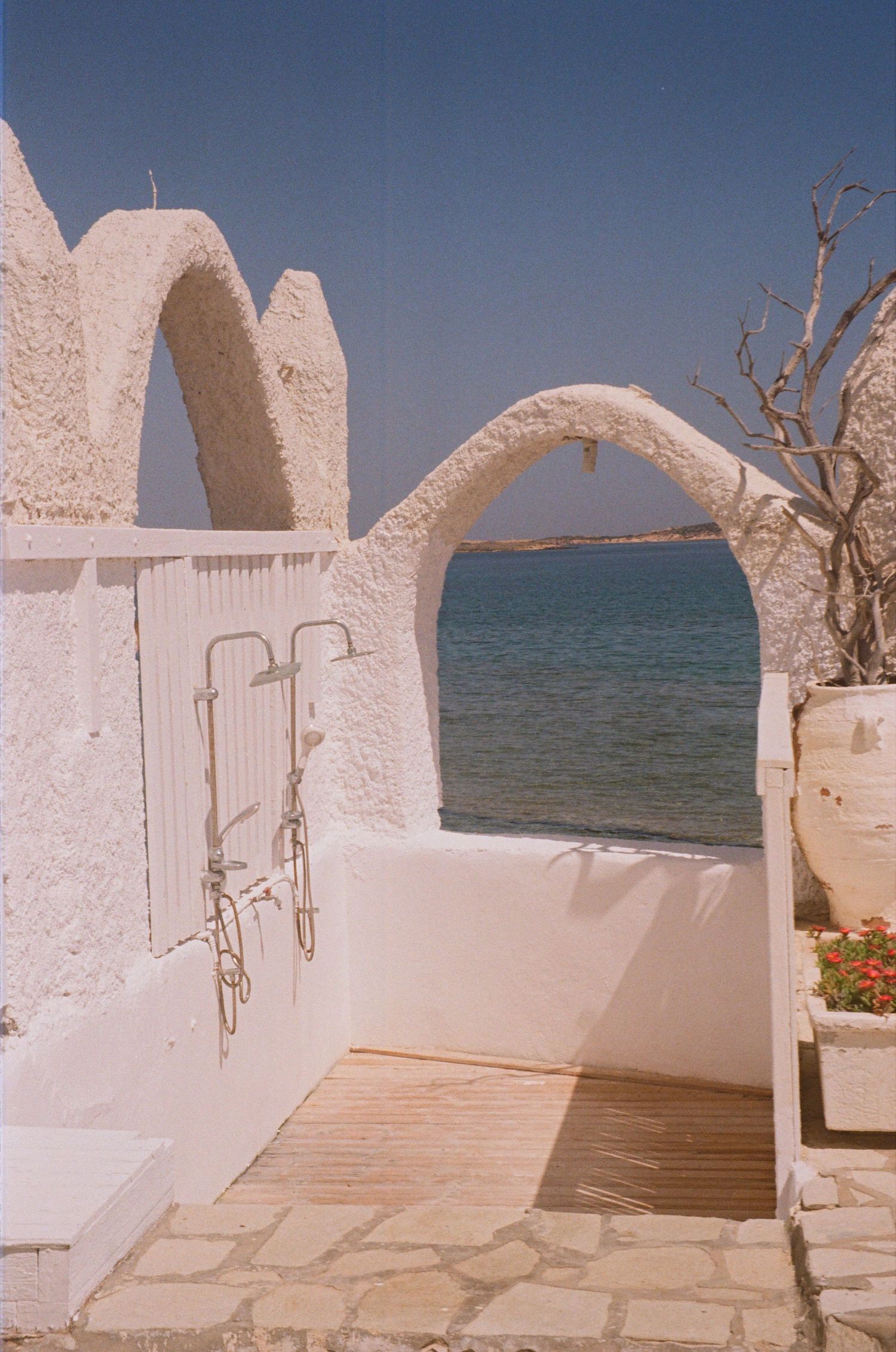 White Cycladic arches frame an outdoor shower overlooking the turquoise Aegean Sea in Greece.