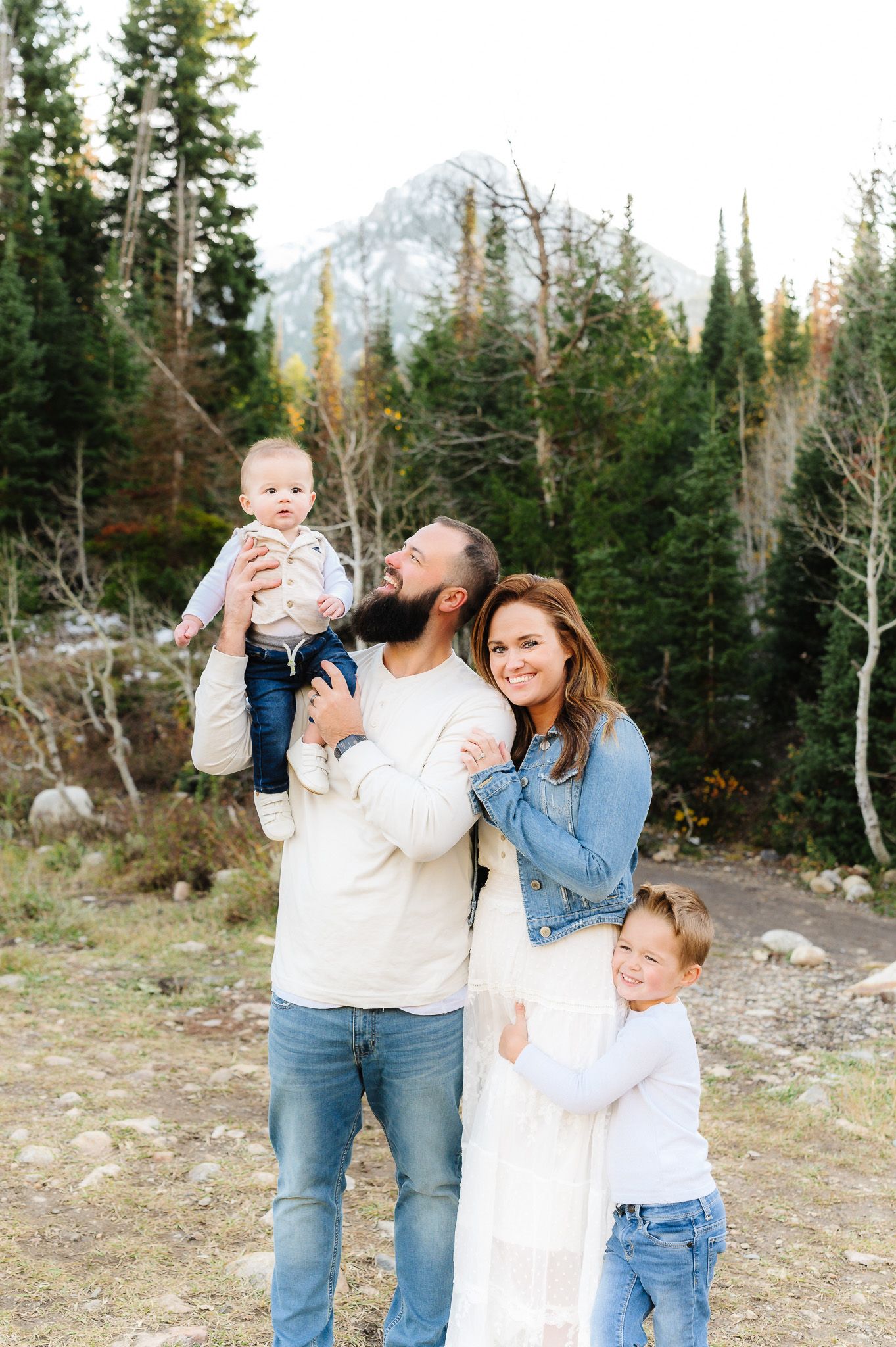 A family shares a joyful moment together outdoors with mountains and evergreen forest in the background.