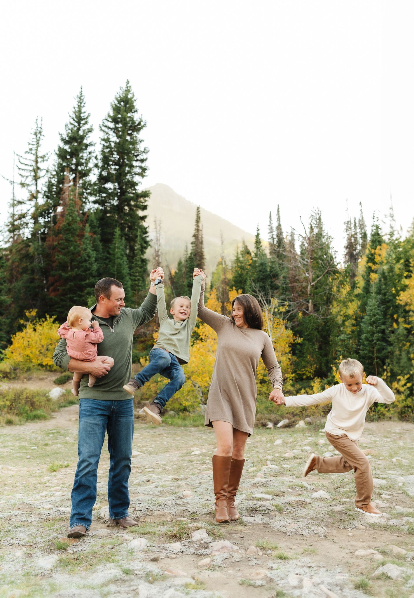 Family members walking hand in hand through mountain terrain with yellow autumn foliage.