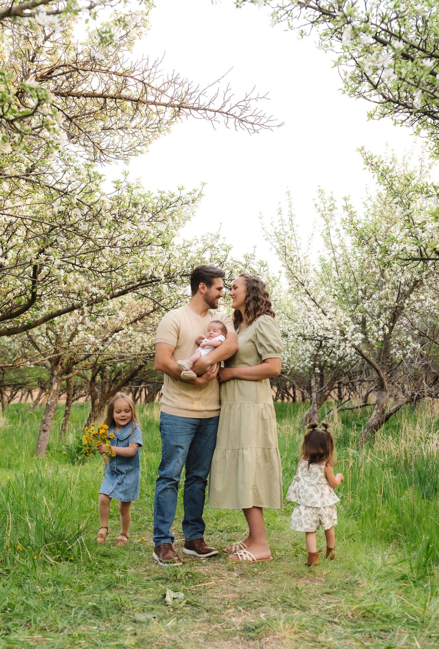 A family shares tender moments together under blooming spring trees in a grassy orchard.
