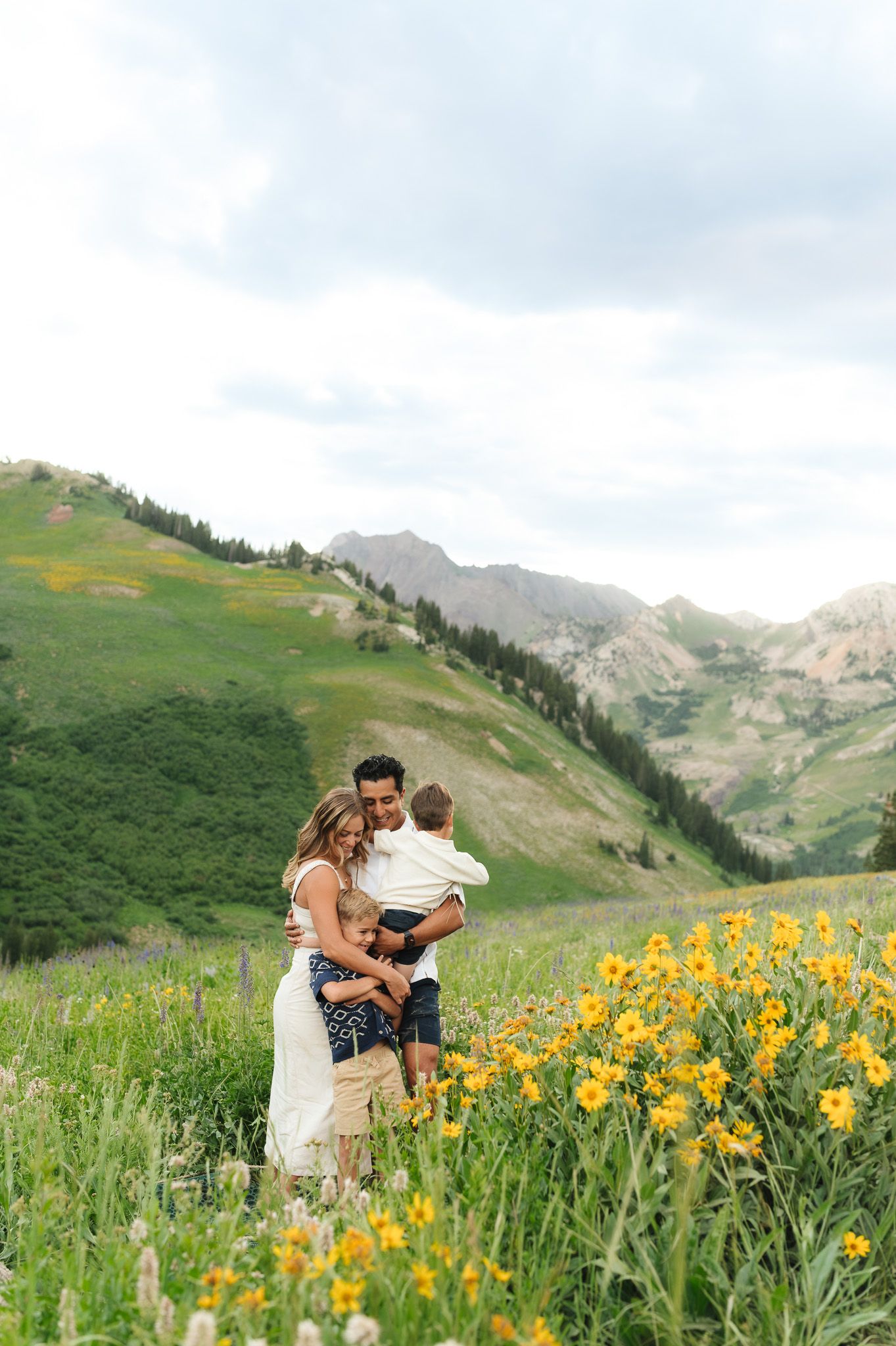 A family stands together among vibrant yellow wildflowers on a scenic mountain slope in summer at Albion Basin in Little Cottonwood Canyon.