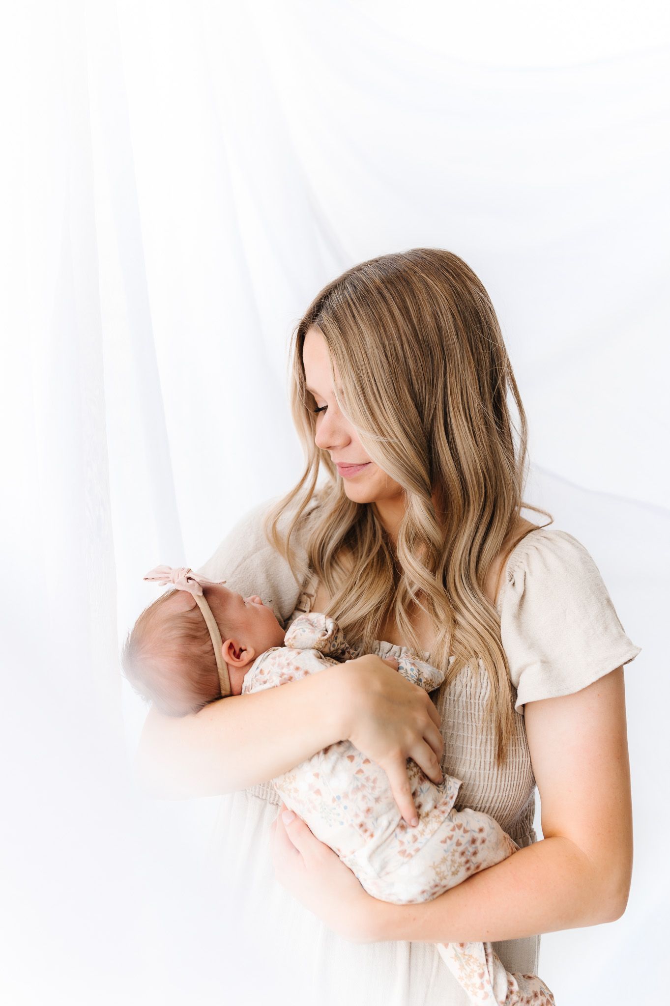Gentle portrait of mother holding newborn in white studio setting.