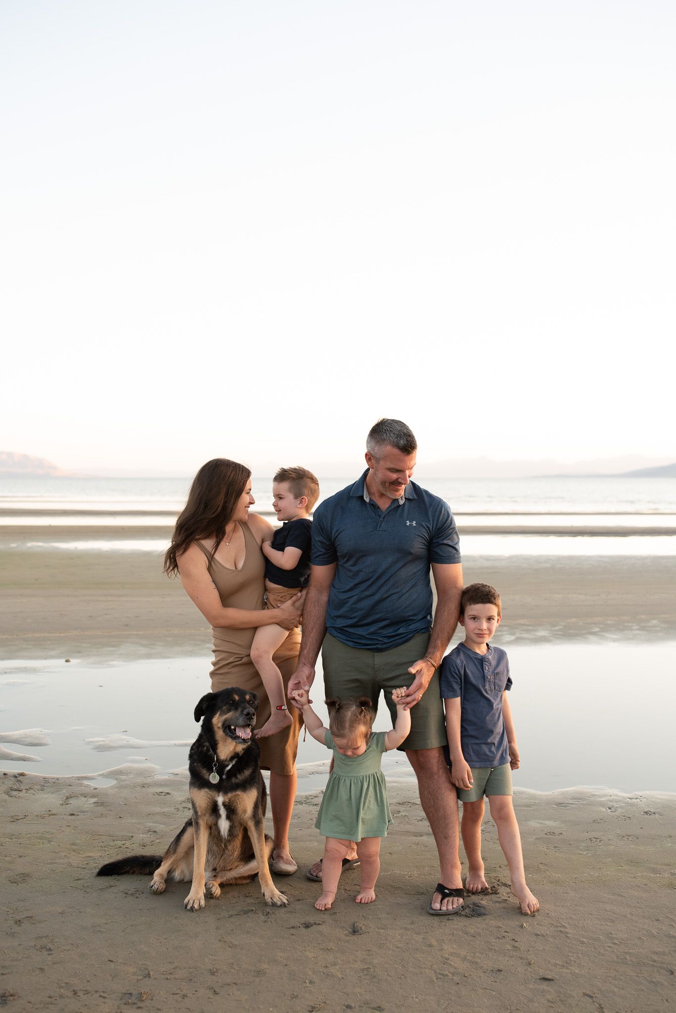 Family and dog pose together on beach at sunset during casual photo session.