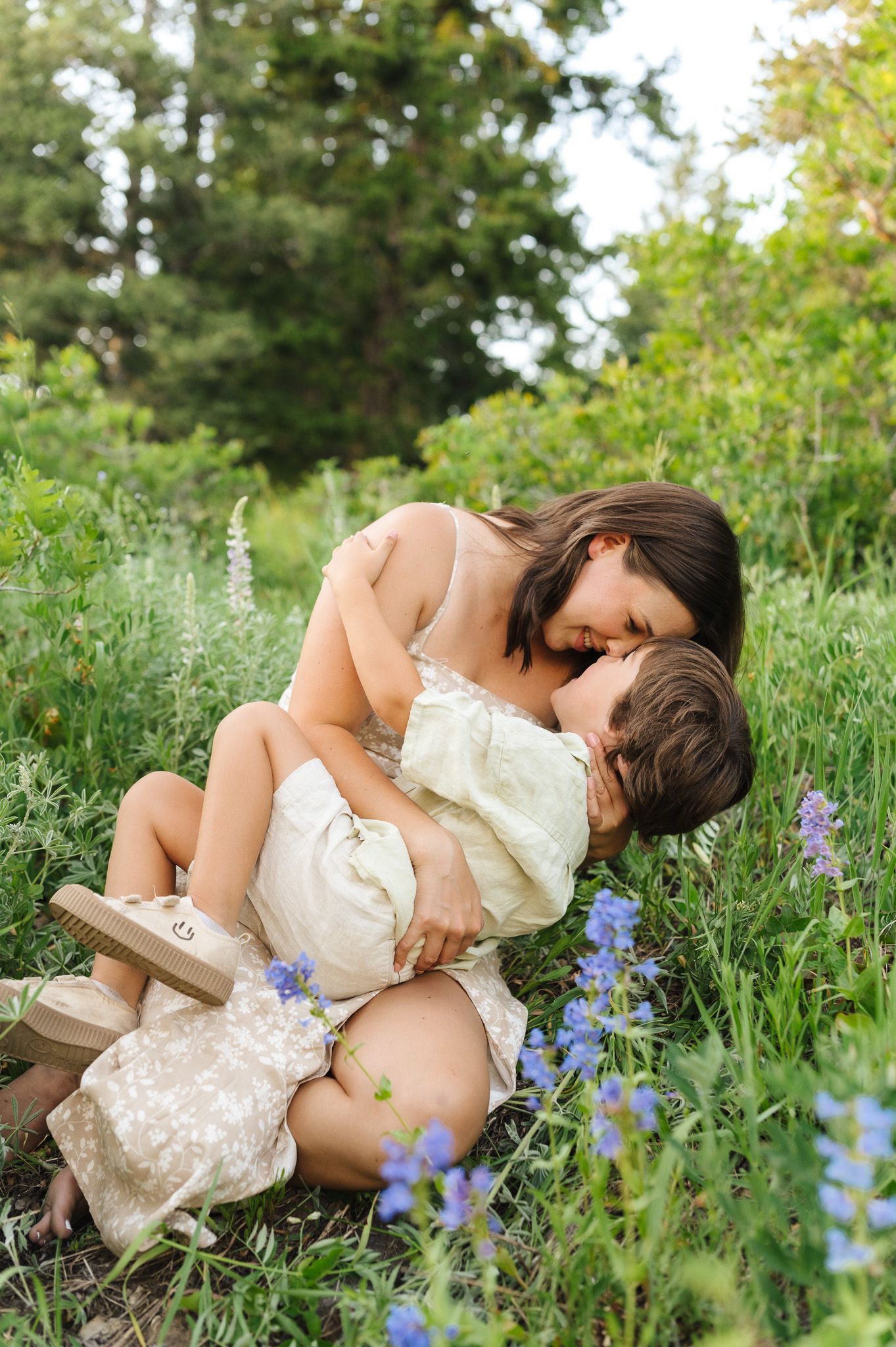Mother and toddler sharing a tender nose kiss while sitting in a lush green meadow with wildflowers.