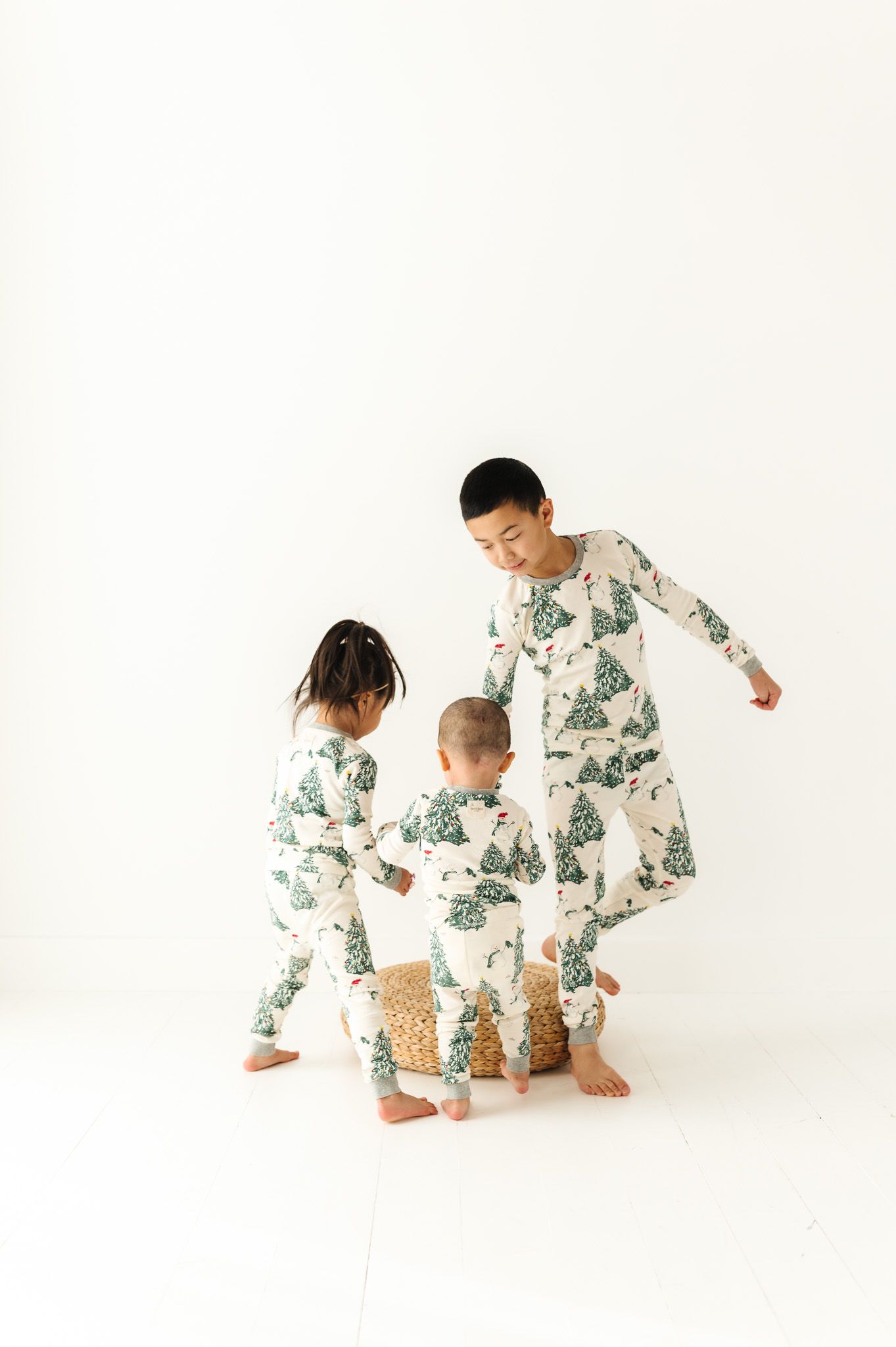 Three children in matching tree-patterned pajamas play together against white background.