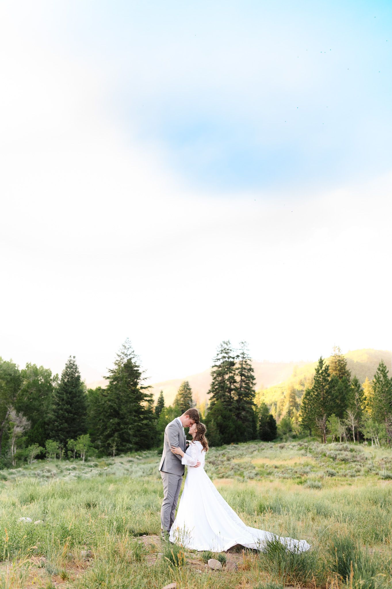 Wedding couple embracing in a scenic mountain meadow at sunset.