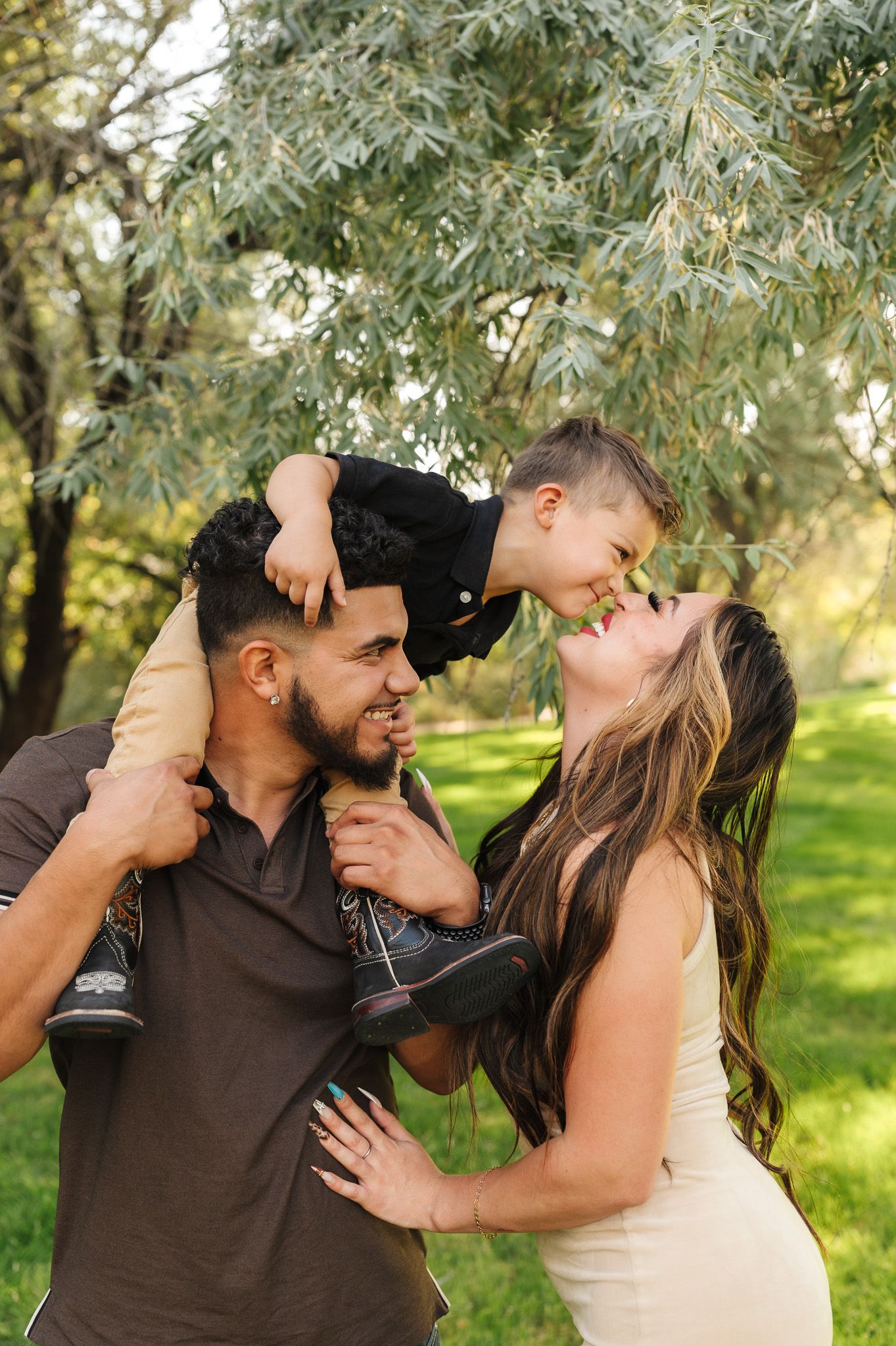 A happy young family with a toddler boy on dad's shoulders sharing a joyful moment outdoors in a lush green park.