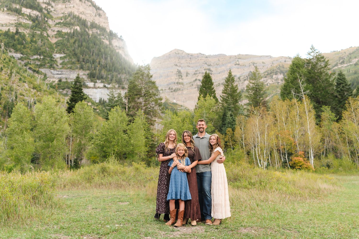 Family of six posing together in a scenic mountain meadow surrounded by aspen trees and rocky cliffs.