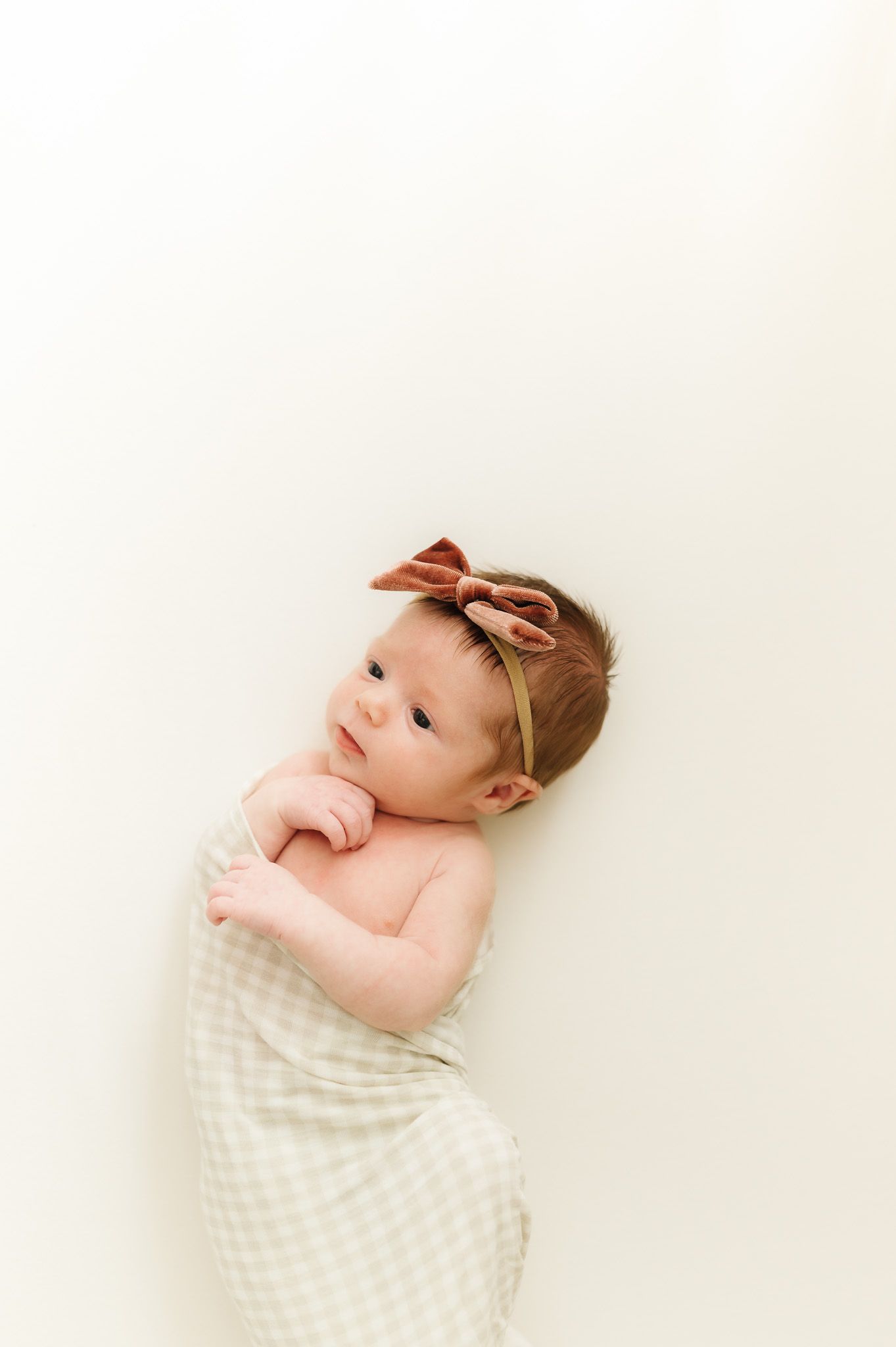 Sweet baby with bow headband swaddled in cream checkered wrap.