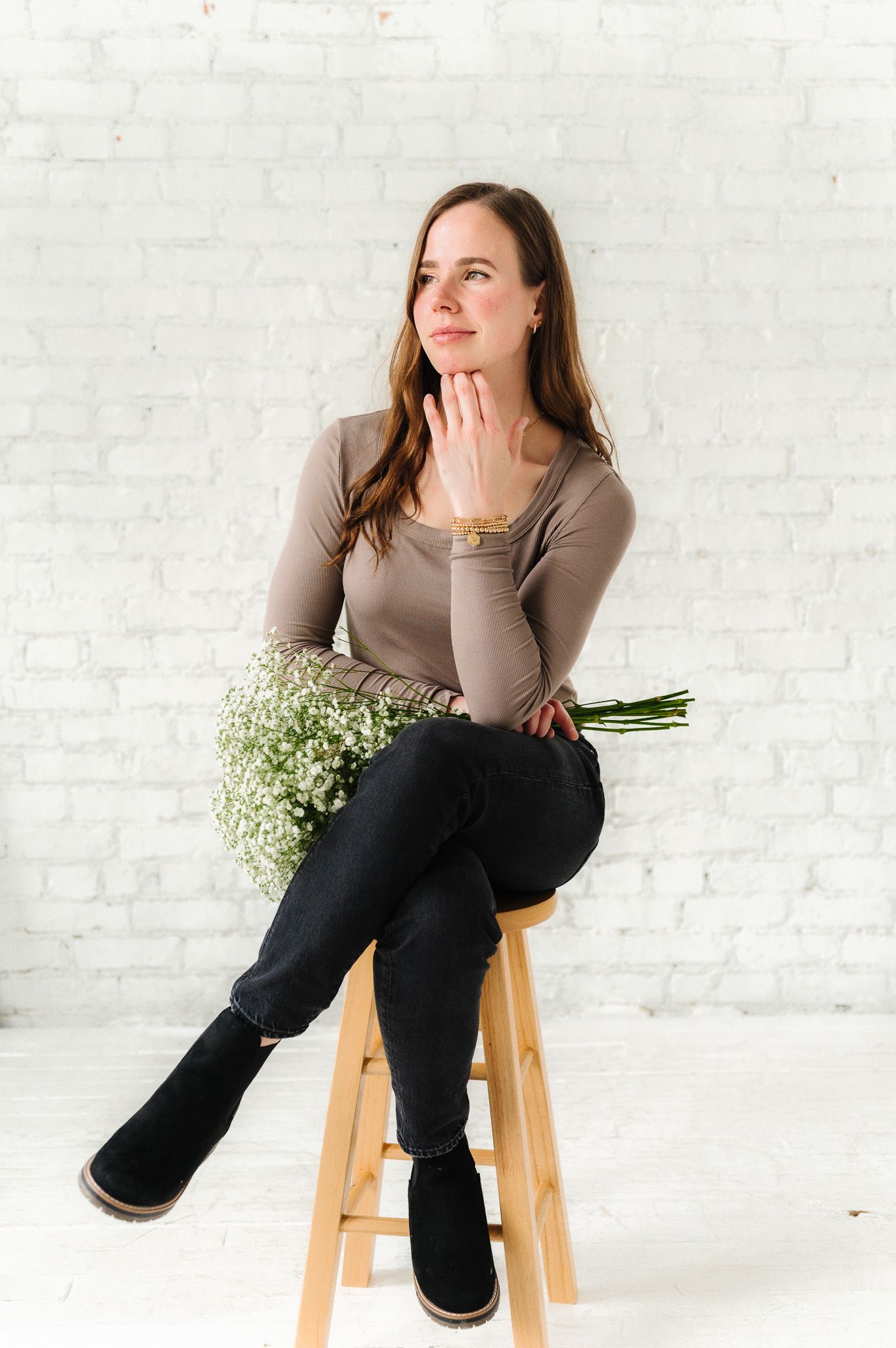Creative portrait with baby's breath flowers on wooden stool against white brick wall.