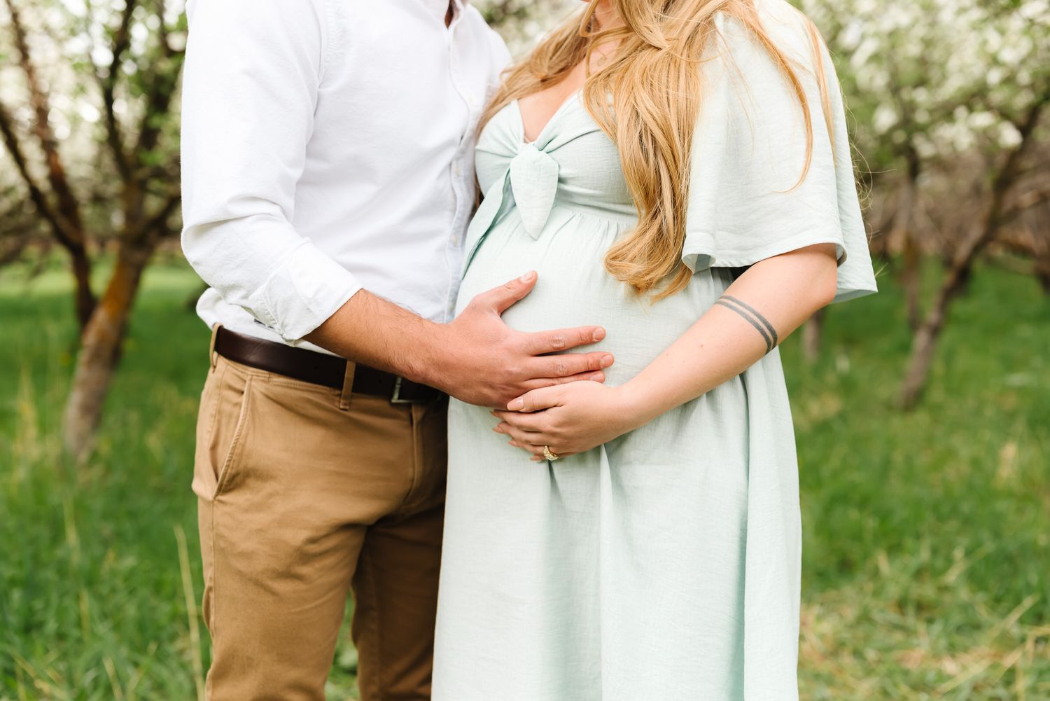 Couple sharing intimate moment in mint dress and khakis among spring blossoms.