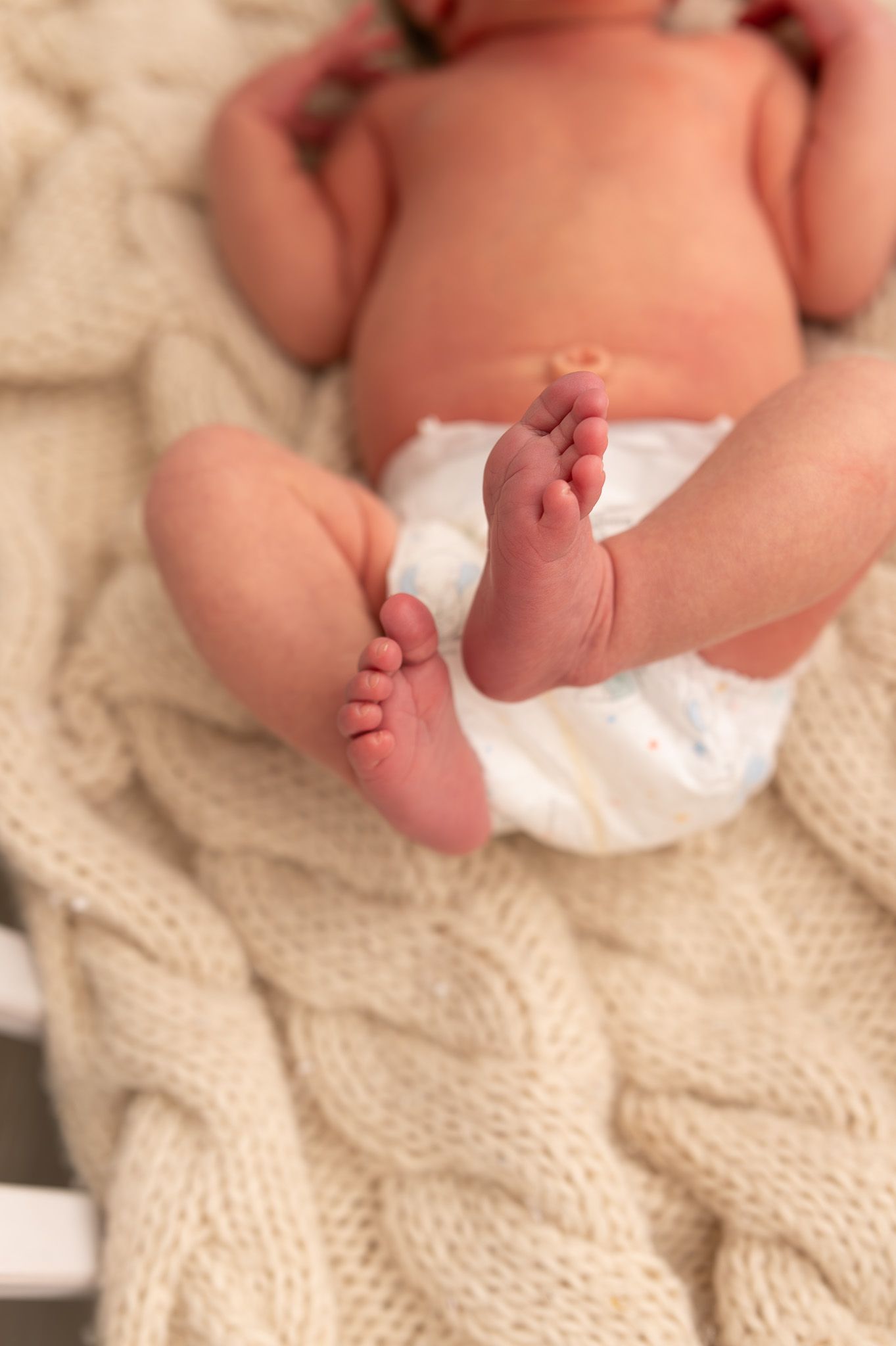 Close-up shots of tiny baby feet resting on a cream-colored knit blanket.