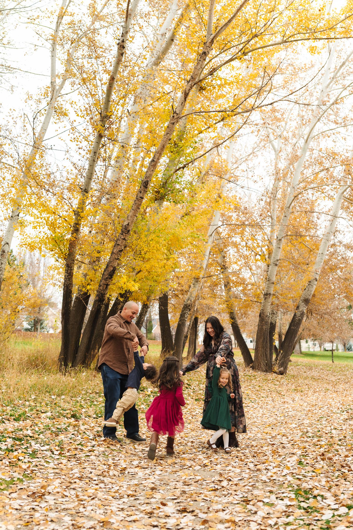 Family playing together on a leaf-covered path surrounded by golden autumn trees.