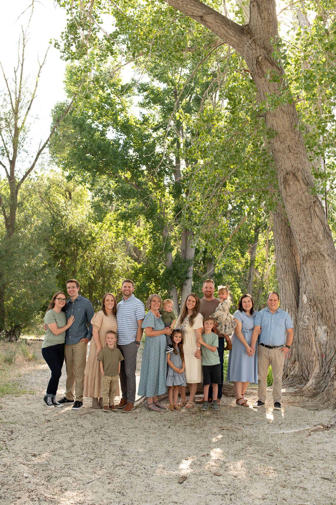 Multi-generational family portrait session under mature trees in natural outdoor setting.