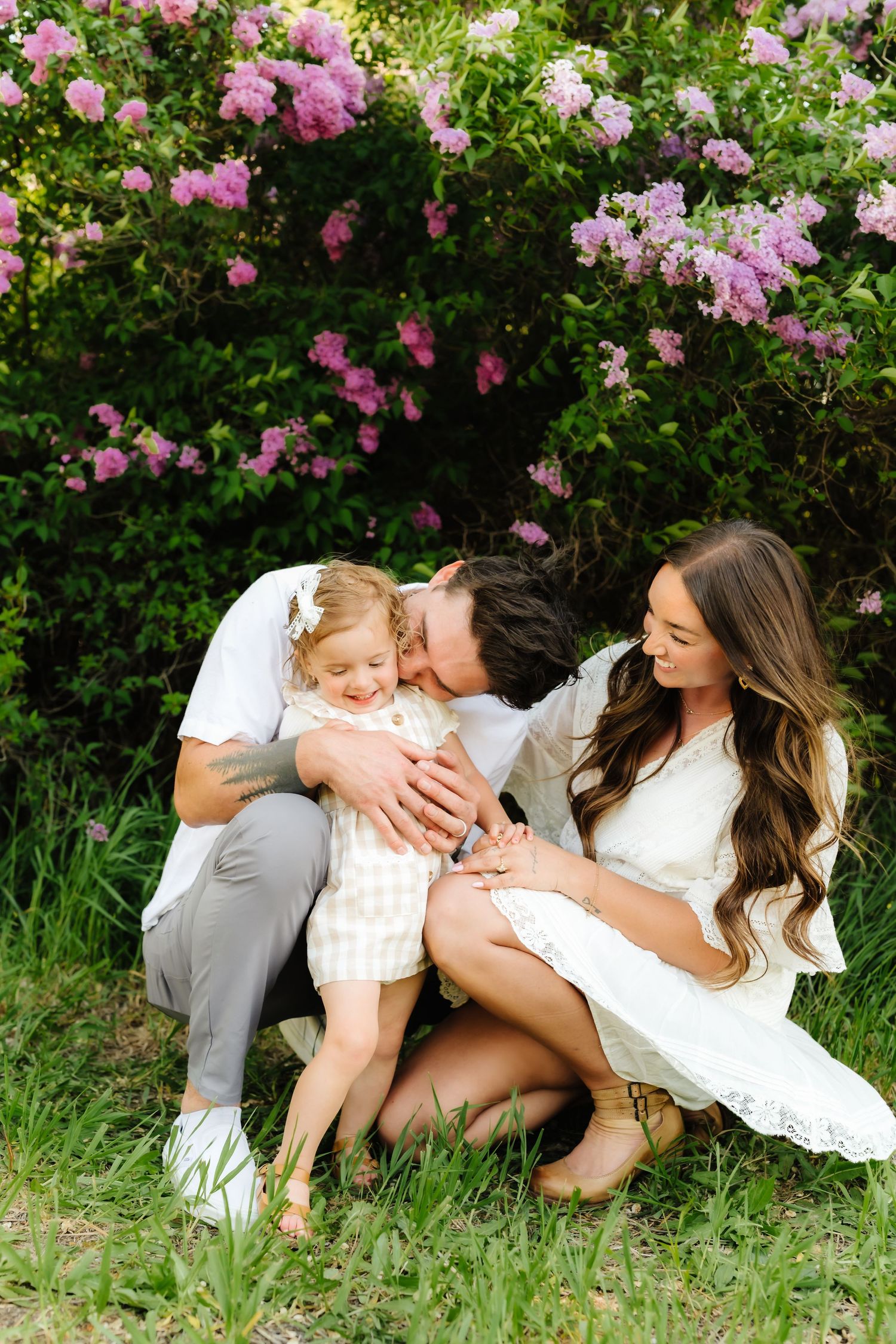 A sweet family moment captured in front of blooming pink roses in a garden.