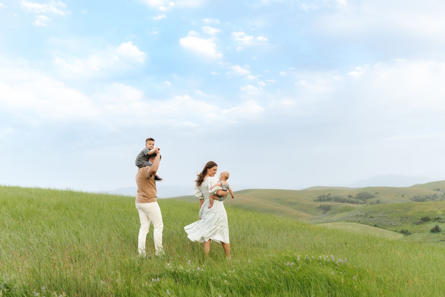 A couple walks through a scenic green hillside meadow with rolling hills in the background on a sunny day.