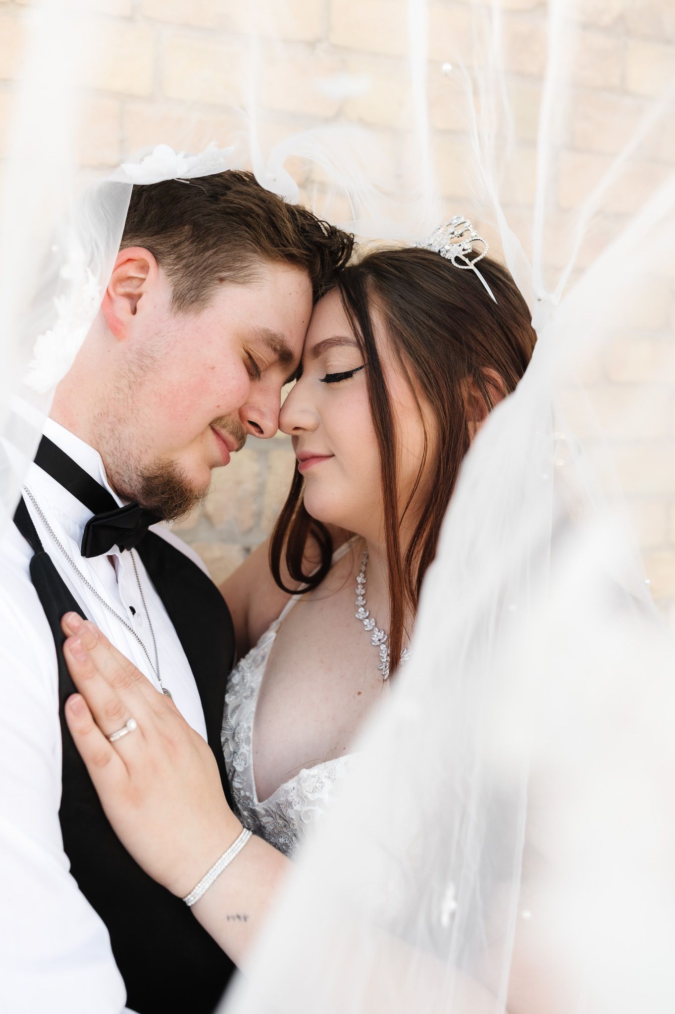 Intimate wedding portrait captures tender moment between couple beneath flowing veil.