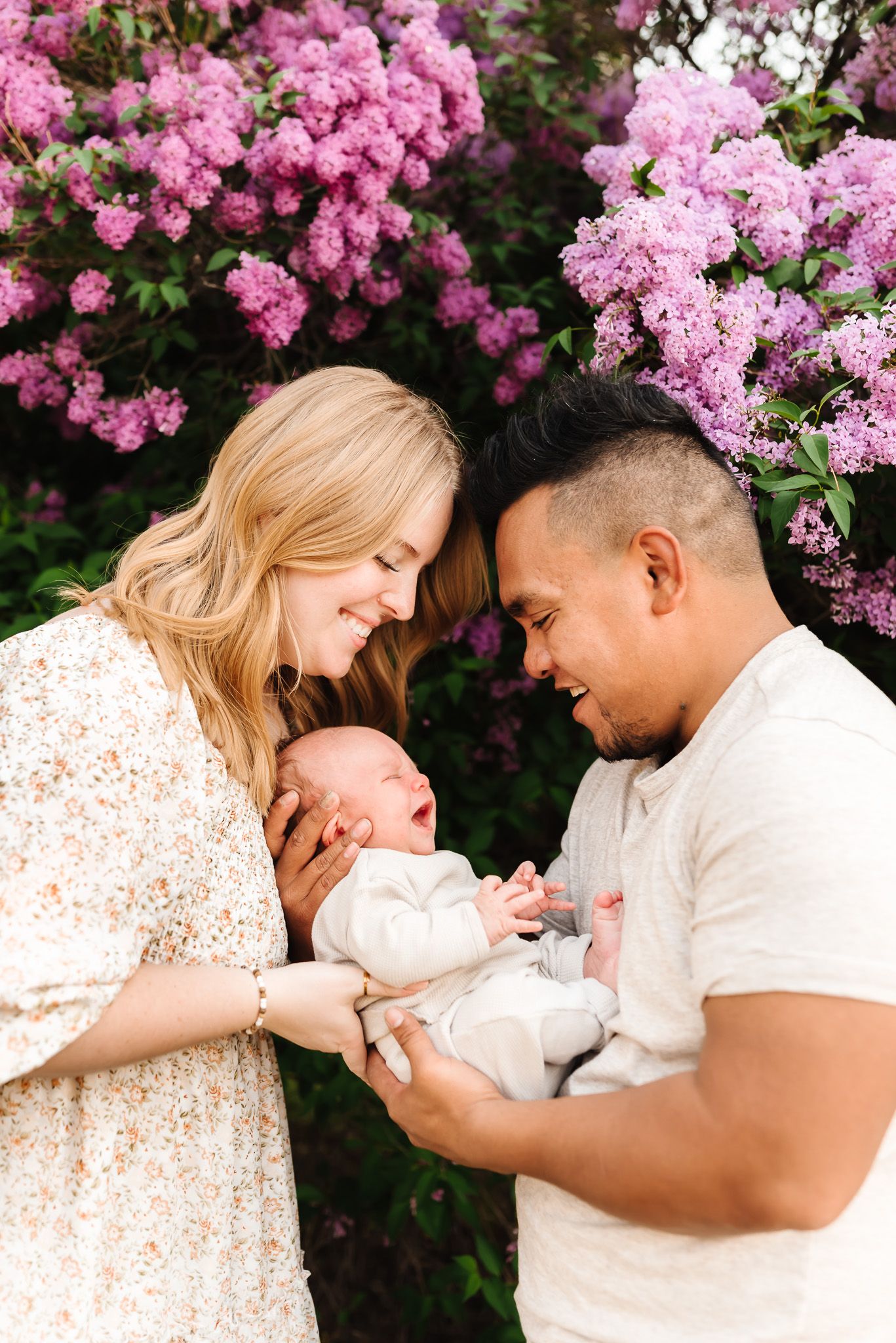 Couple sharing tender moments with newborn against backdrop of pink flowering trees.