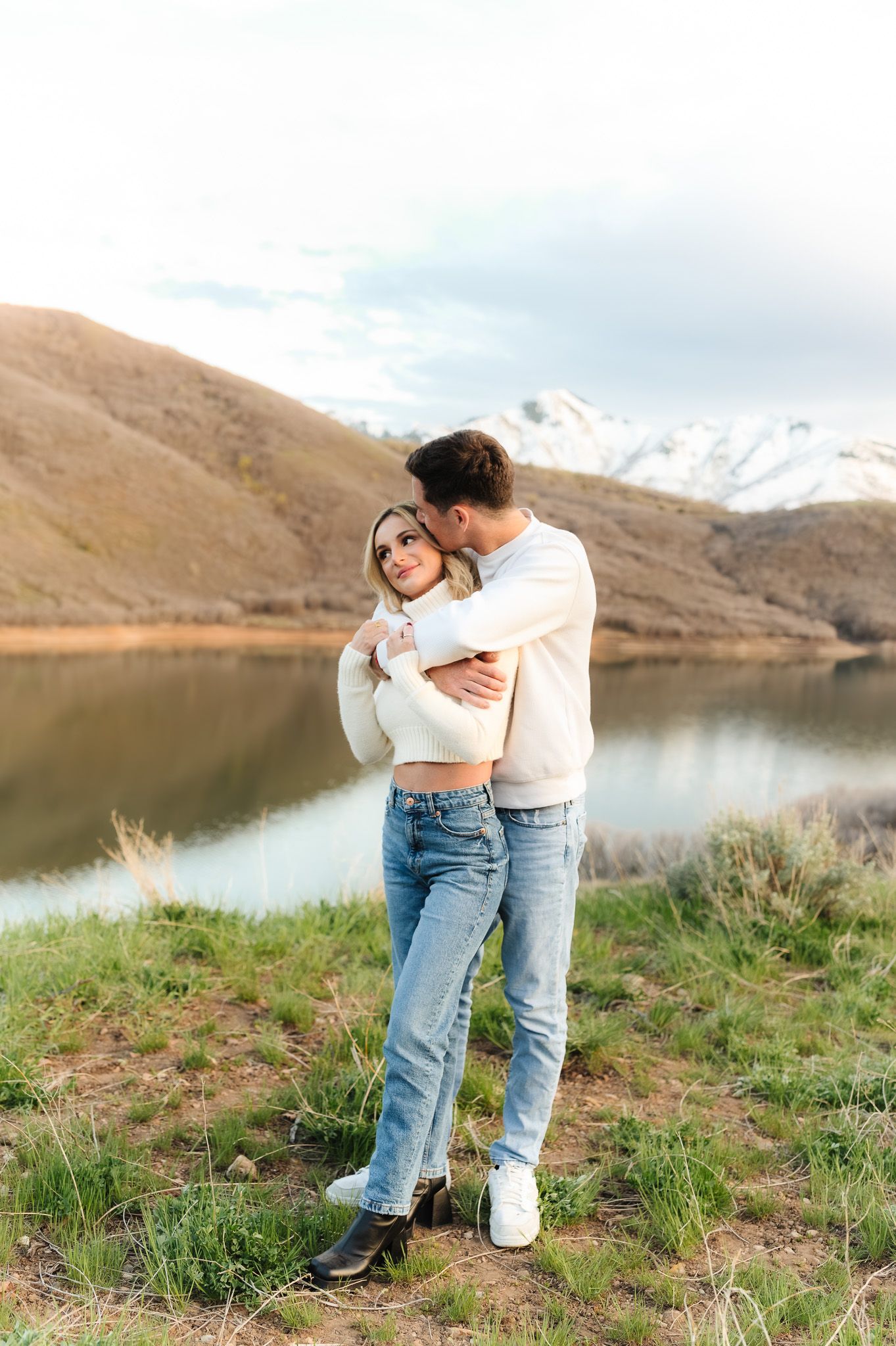 Couple in coordinated outfits sharing affectionate moments near a mountain reservoir.