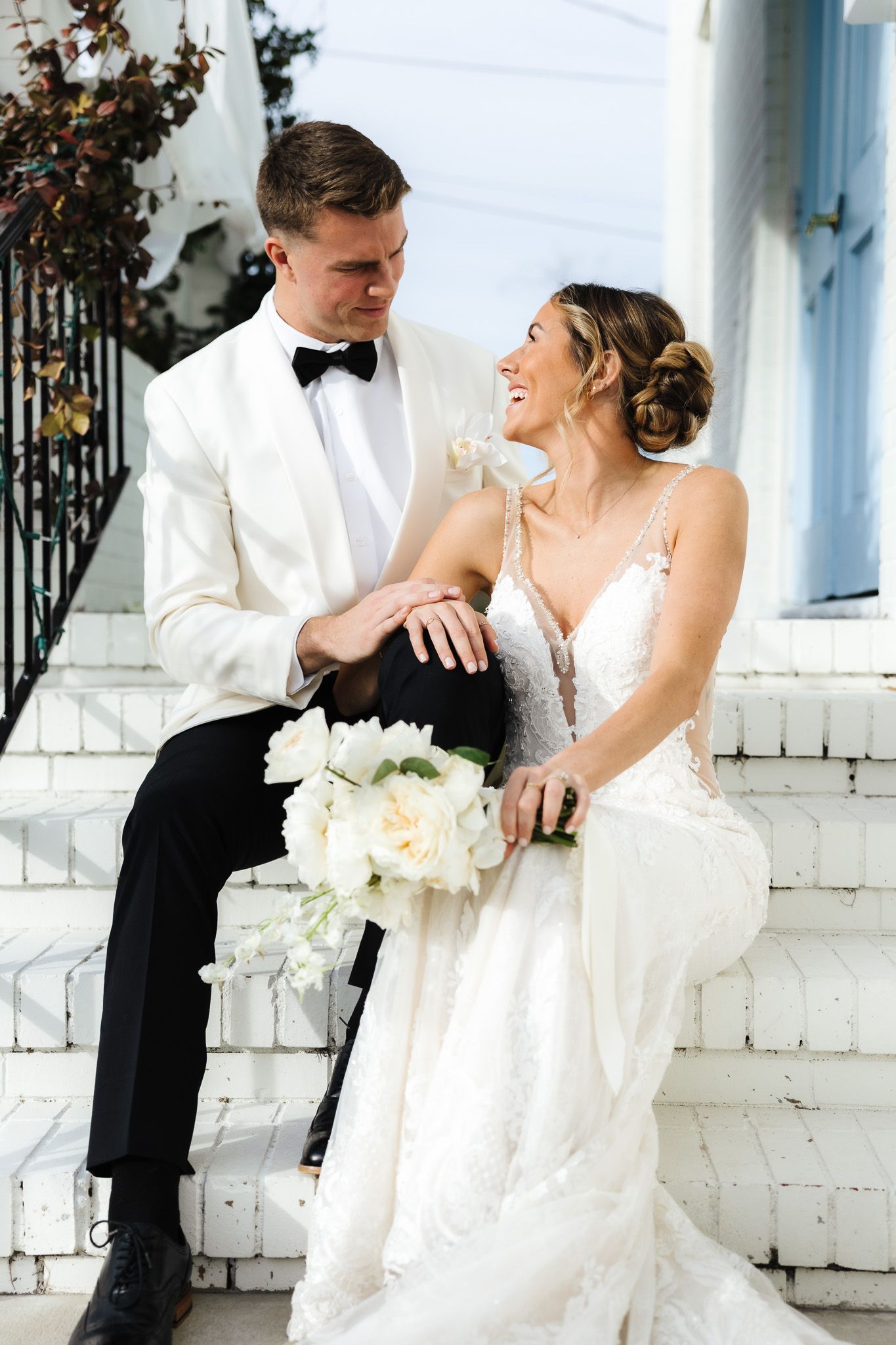Wedding couple sharing intimate moment on white porch with classic architecture.