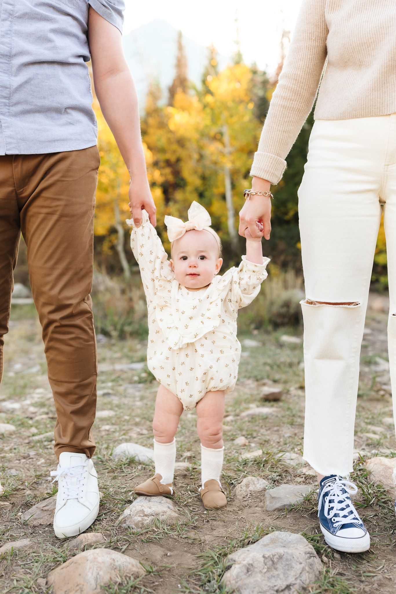 Close-up of family members' legs and feet with small child reaching up on rocky ground.