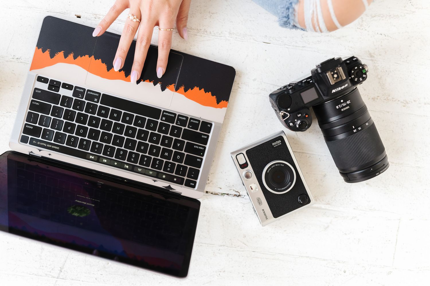 Flatlay of photography equipment including laptop, camera and keyboard on white background.