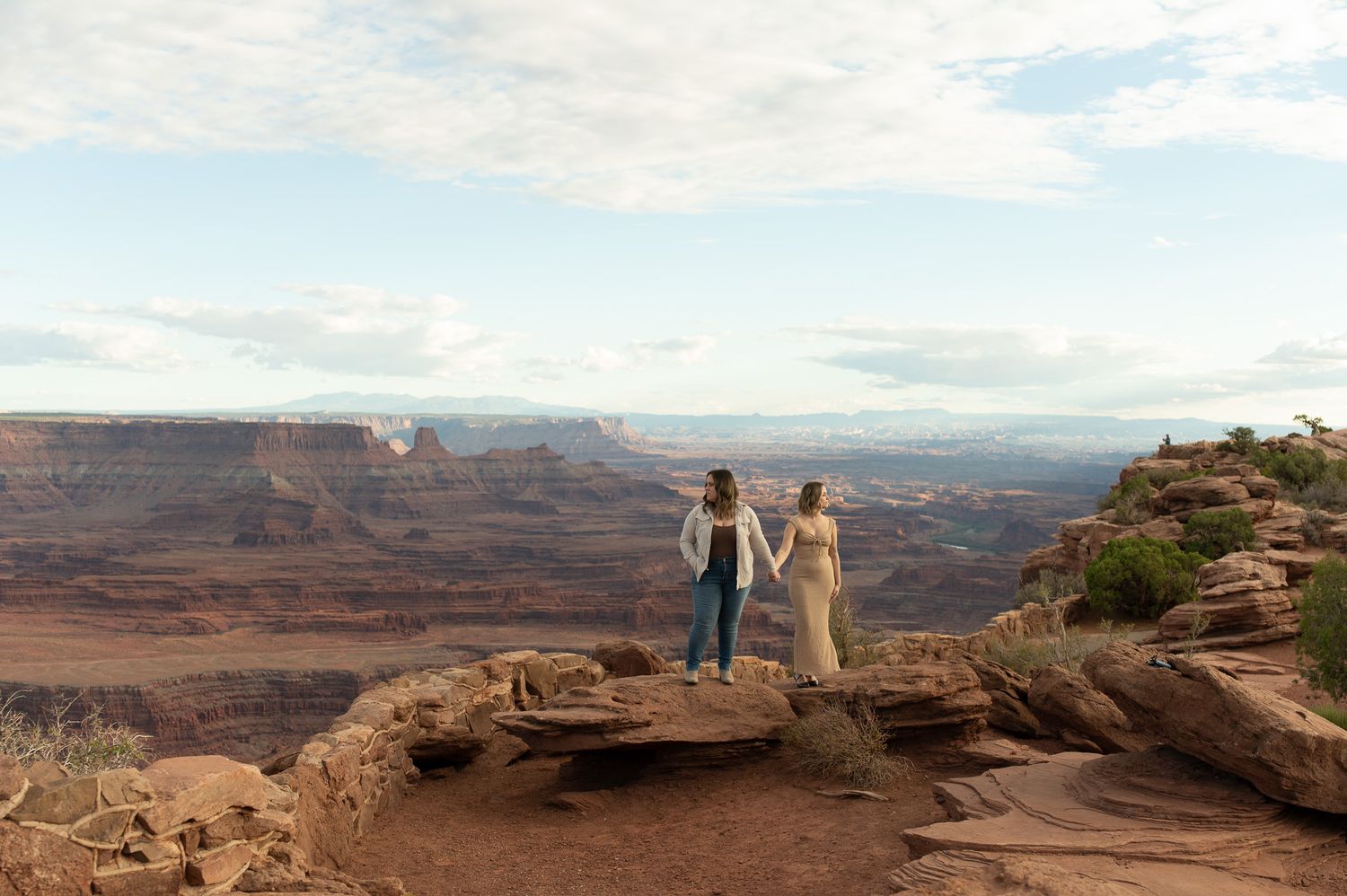 Couple holding hands on a rocky overlook with stunning canyon landscape views in the background.