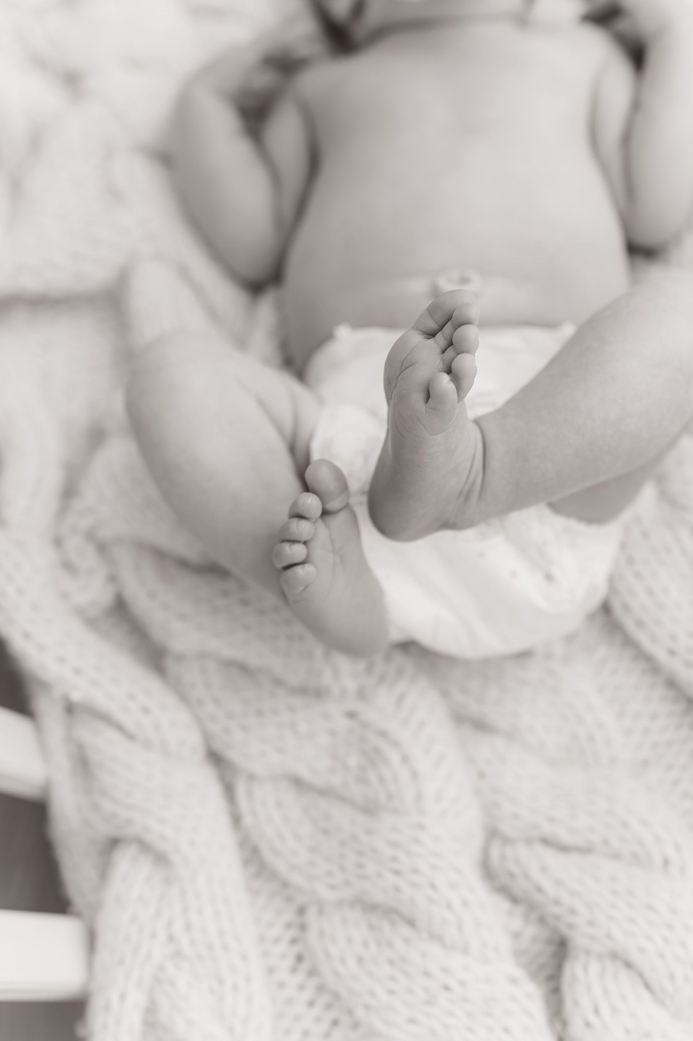 Close-up of tiny baby feet wrapped in soft white knitted blanket.