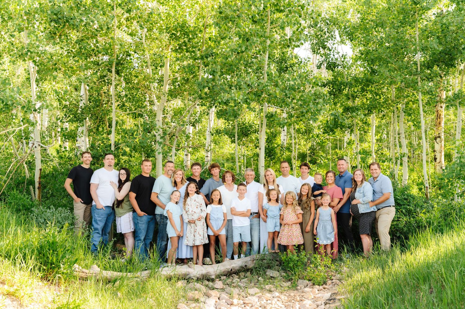 Extended family gathered for a portrait session in a lush green forest setting.