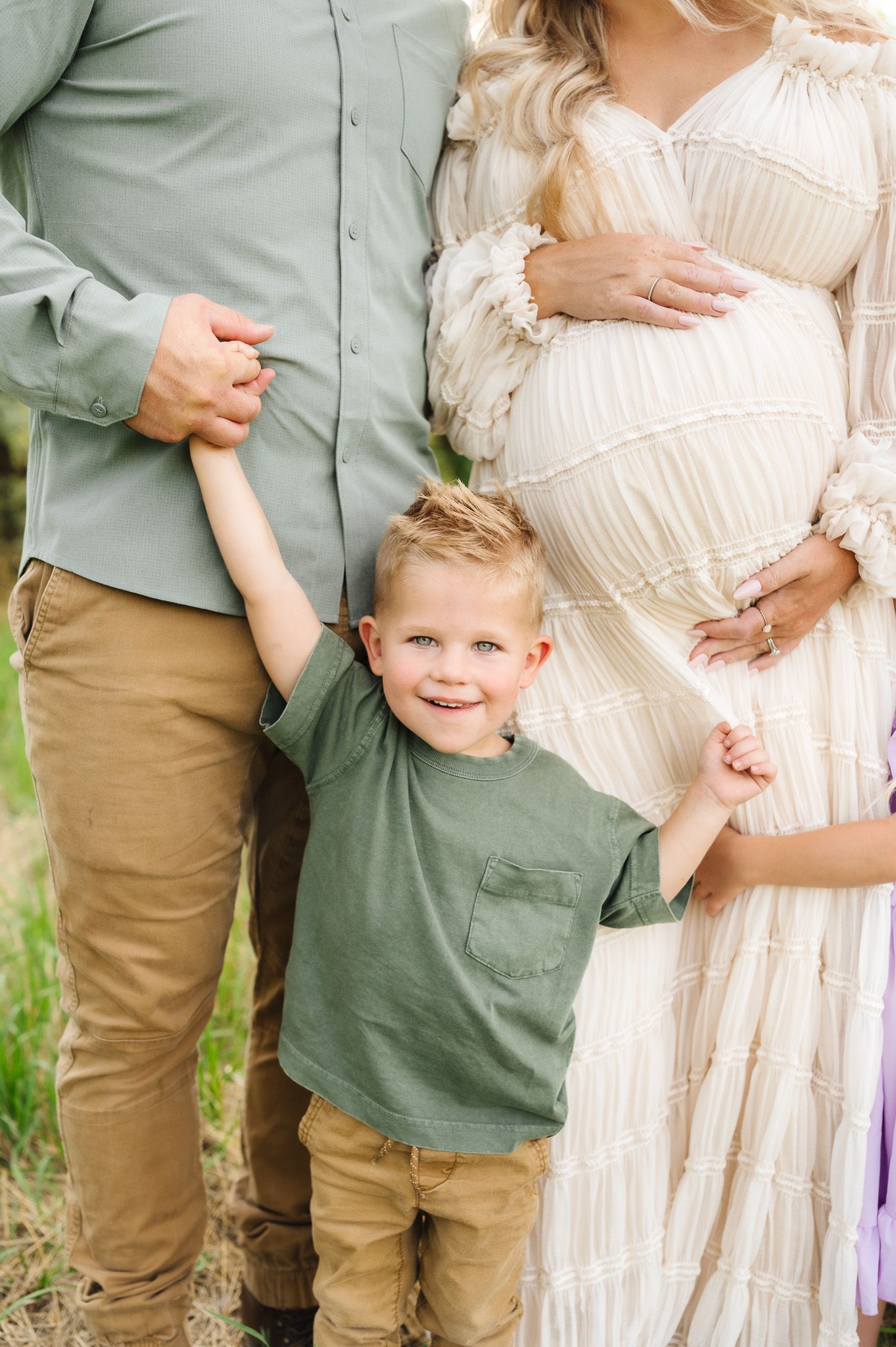 Family maternity photo with coordinating sage green and cream outfits in outdoor setting.