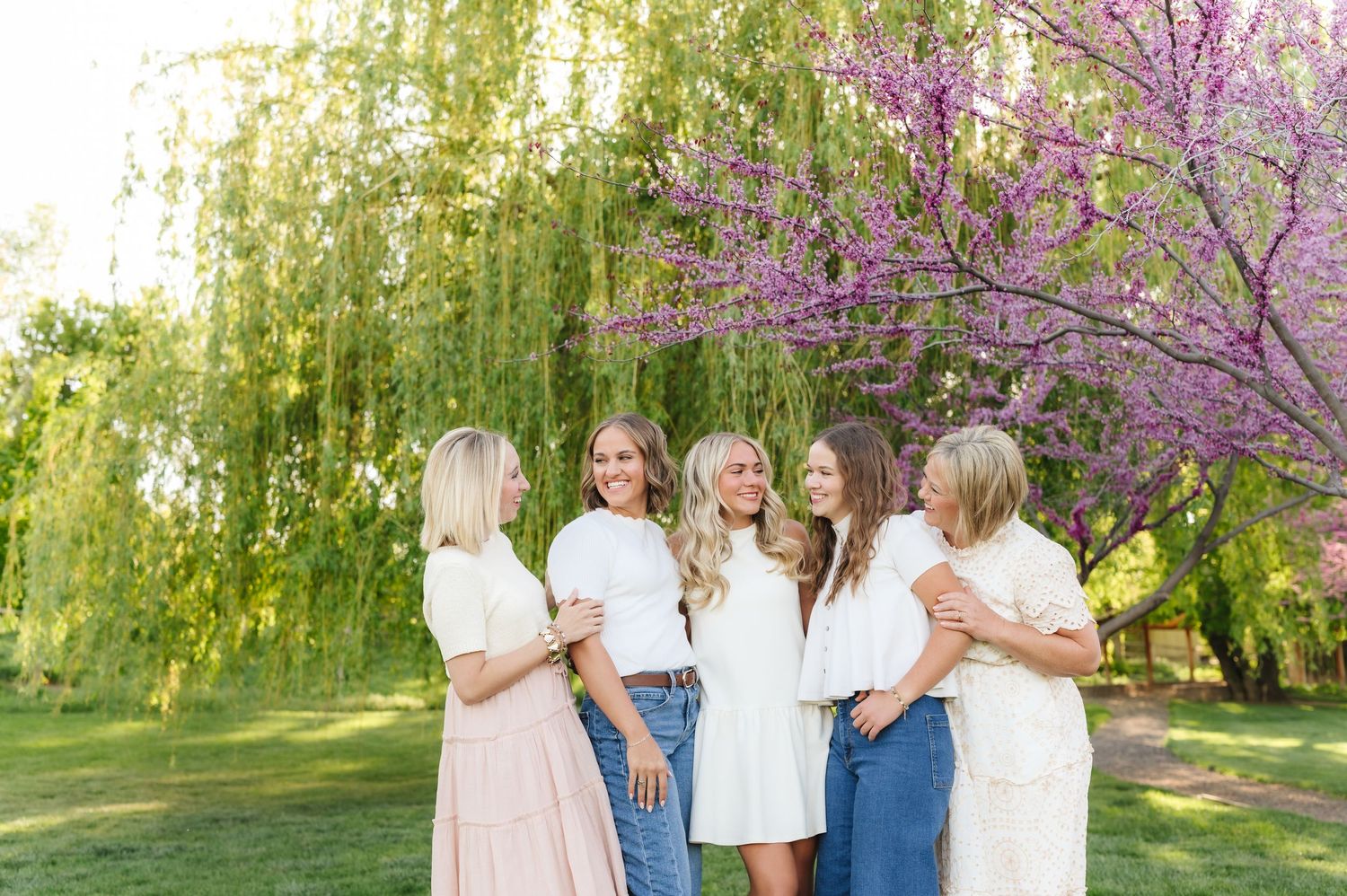A group stands together in a blooming spring garden with pink cherry blossoms and weeping willow trees.