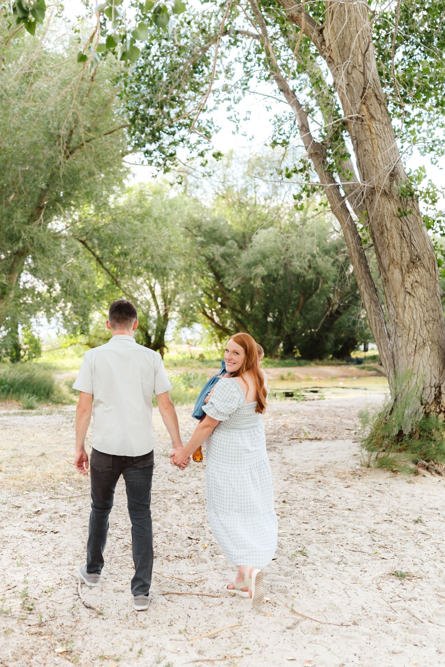 Couple walking hand in hand through a scenic tree-lined path outdoors.