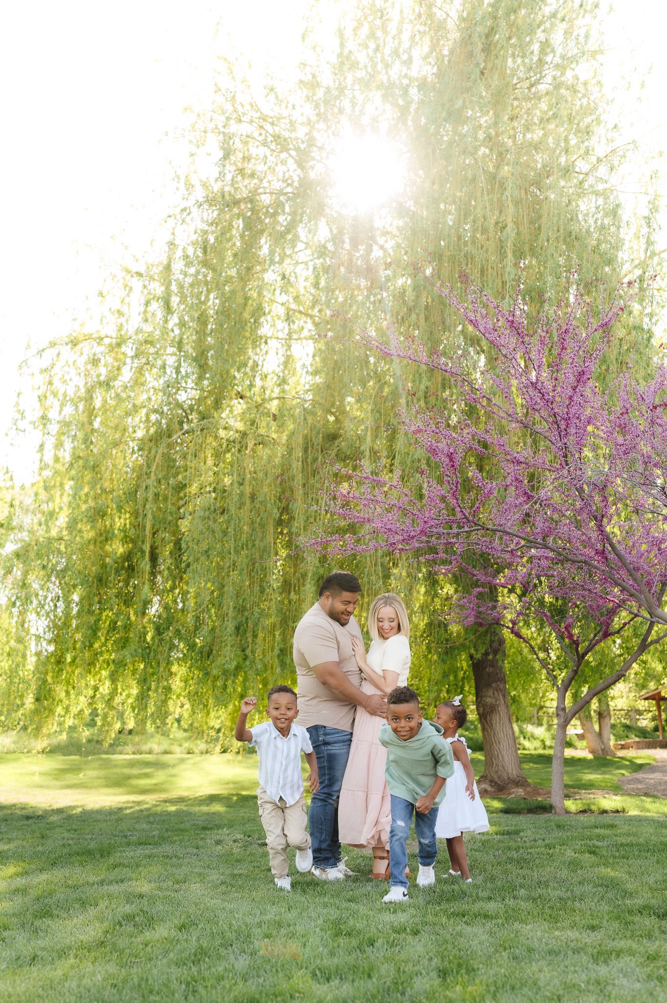 Family of five enjoying a sunny spring day in a lush green park with blooming trees.