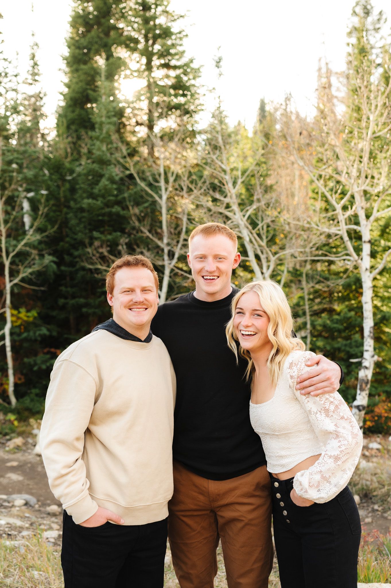Group wearing coordinated neutral colors poses casually against mountain forest backdrop.