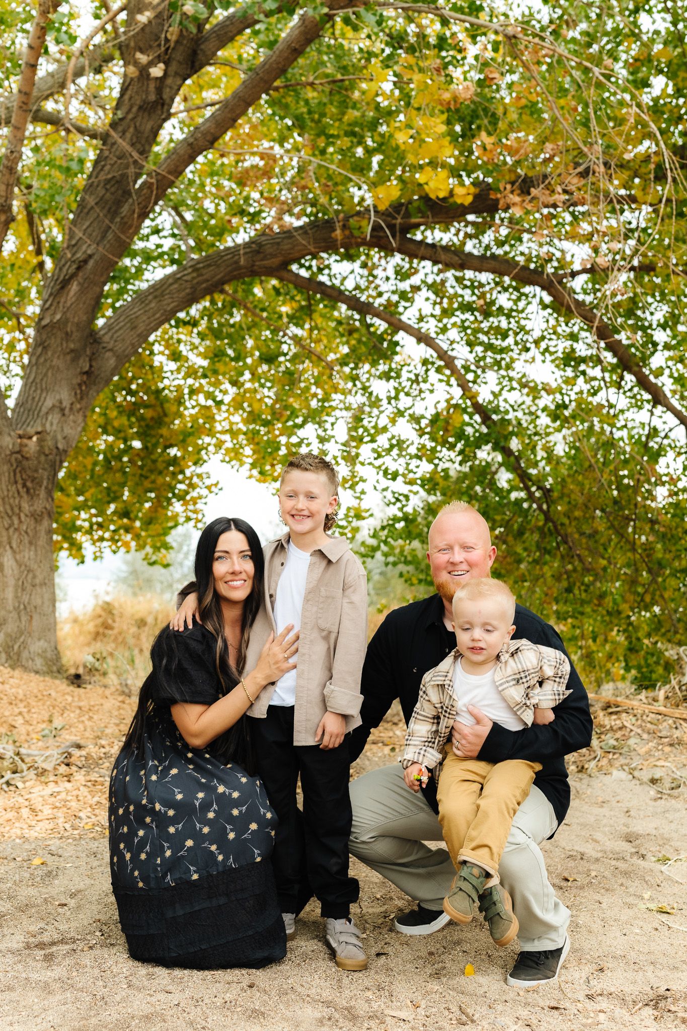 Family sitting together under trees with golden autumn leaves.