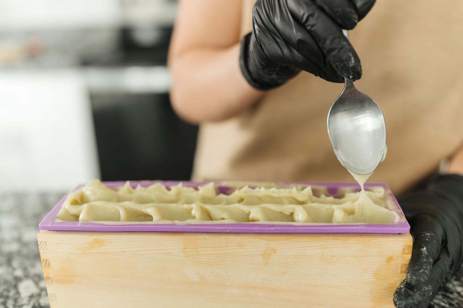 A chef wearing black gloves carefully spreads a layer of frosting onto a cake with a metal spatula.