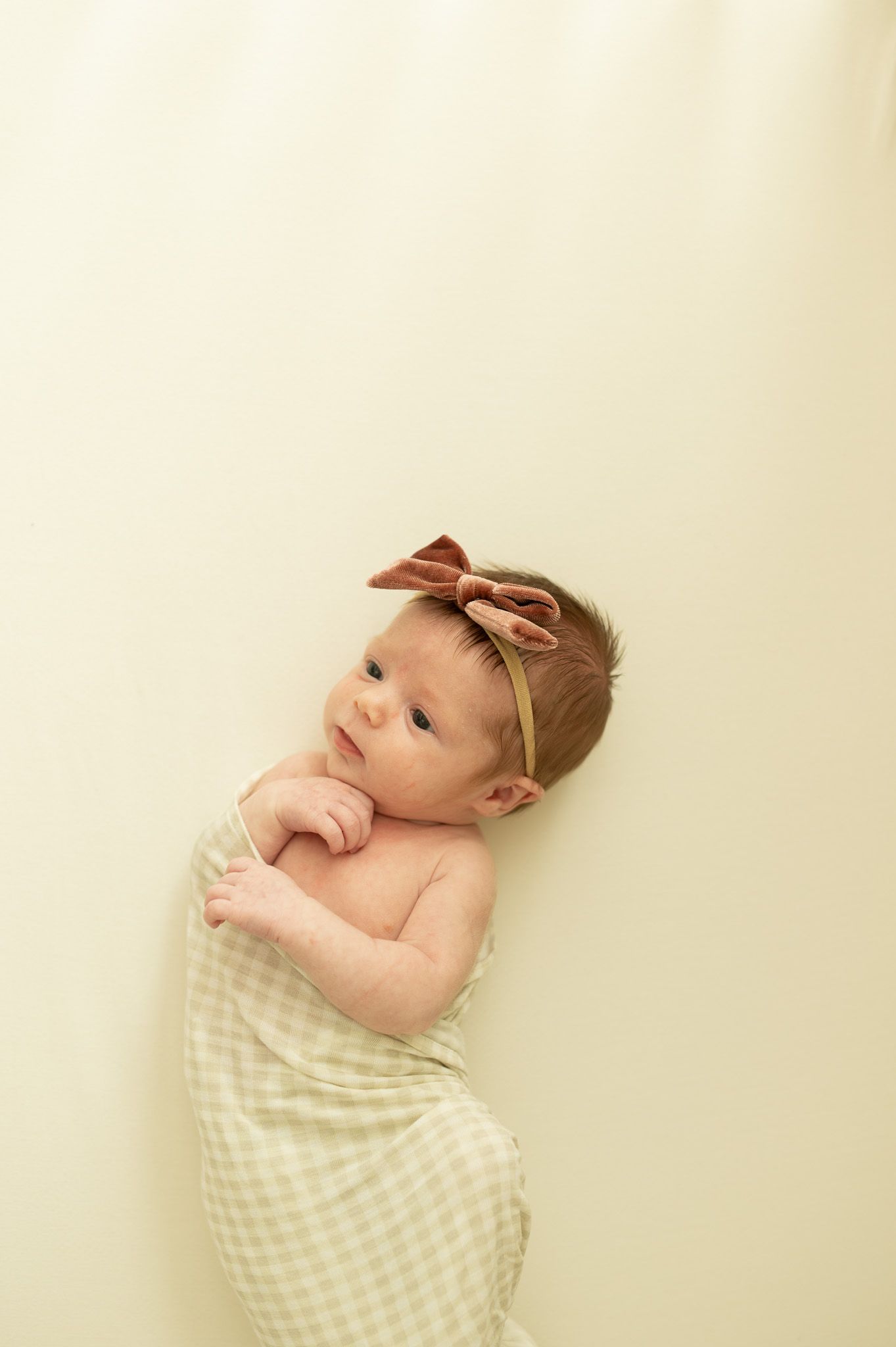 Newborn baby wrapped in checkered blanket on cream background.