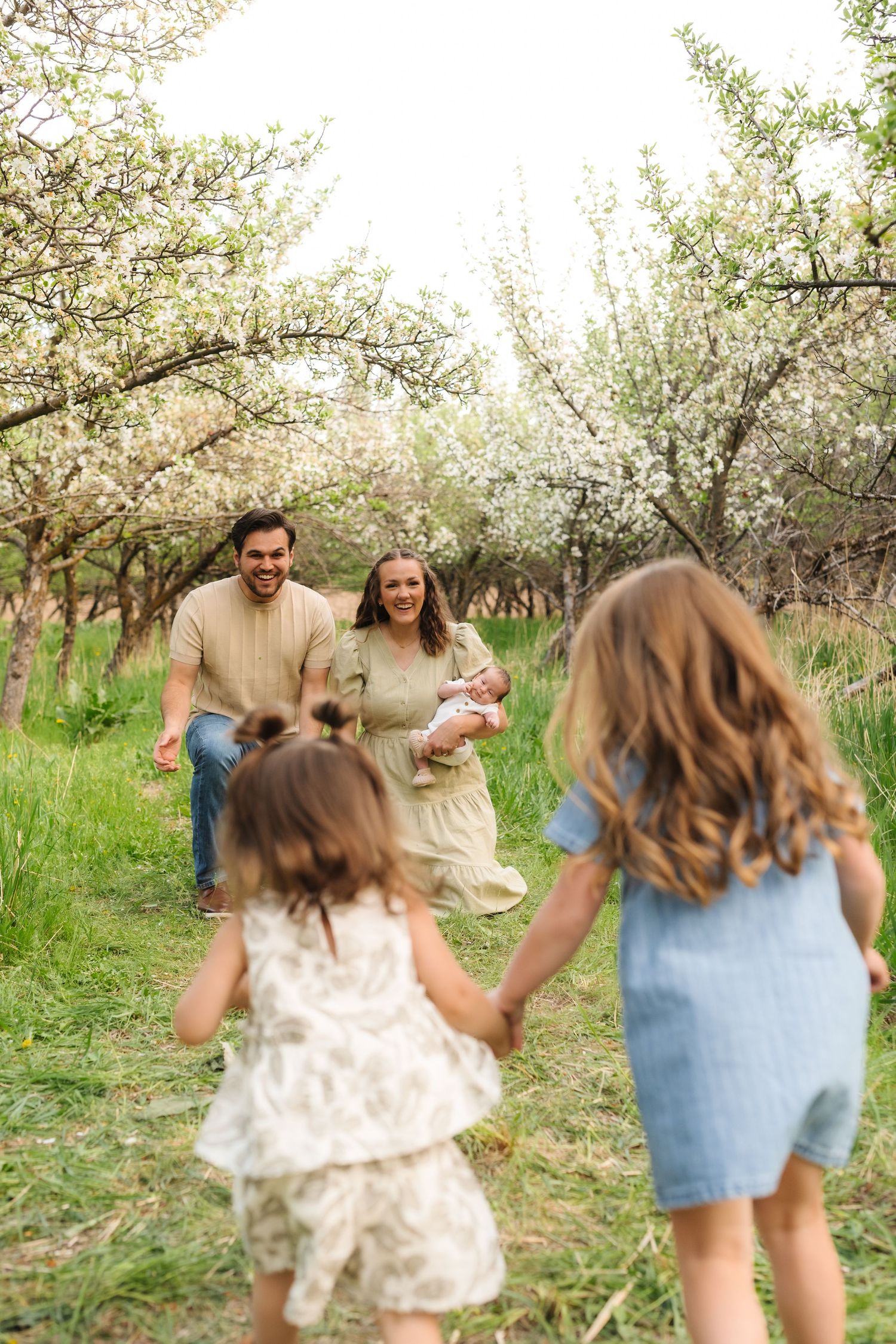 A group enjoys a playful moment in a blooming spring orchard with white flowers and green grass.