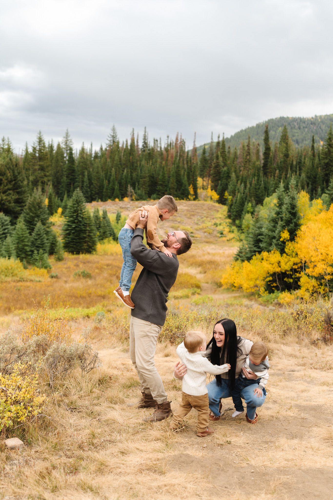 Family playing and posing together on mountain trail with autumn foliage in background.
