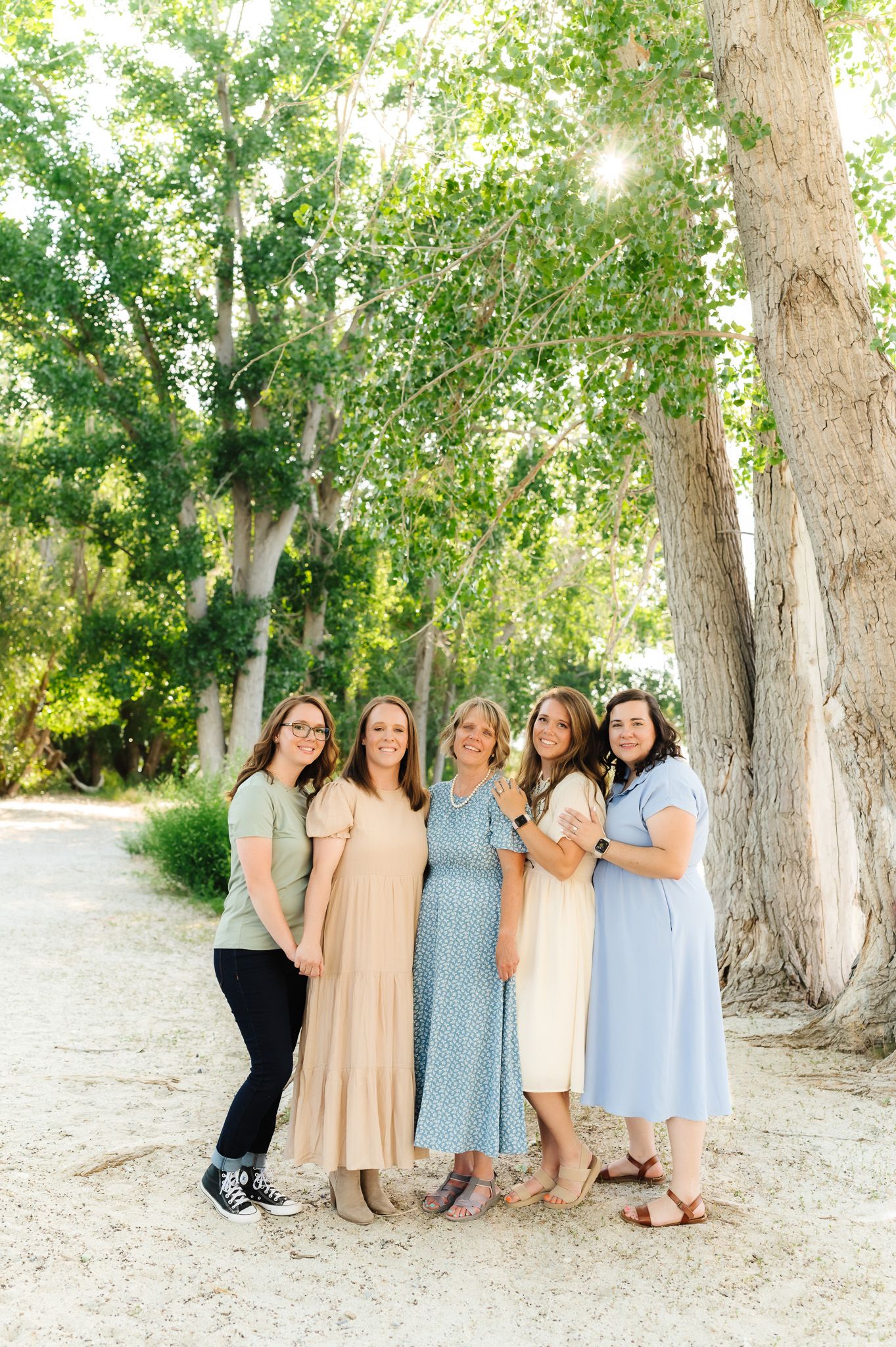 Group poses casually together under tall trees in coordinated pastel dresses.