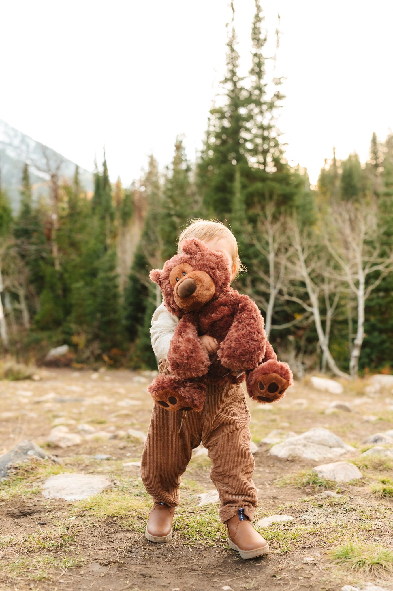 Child in brown overalls playing and exploring outdoors in a mountain landscape.