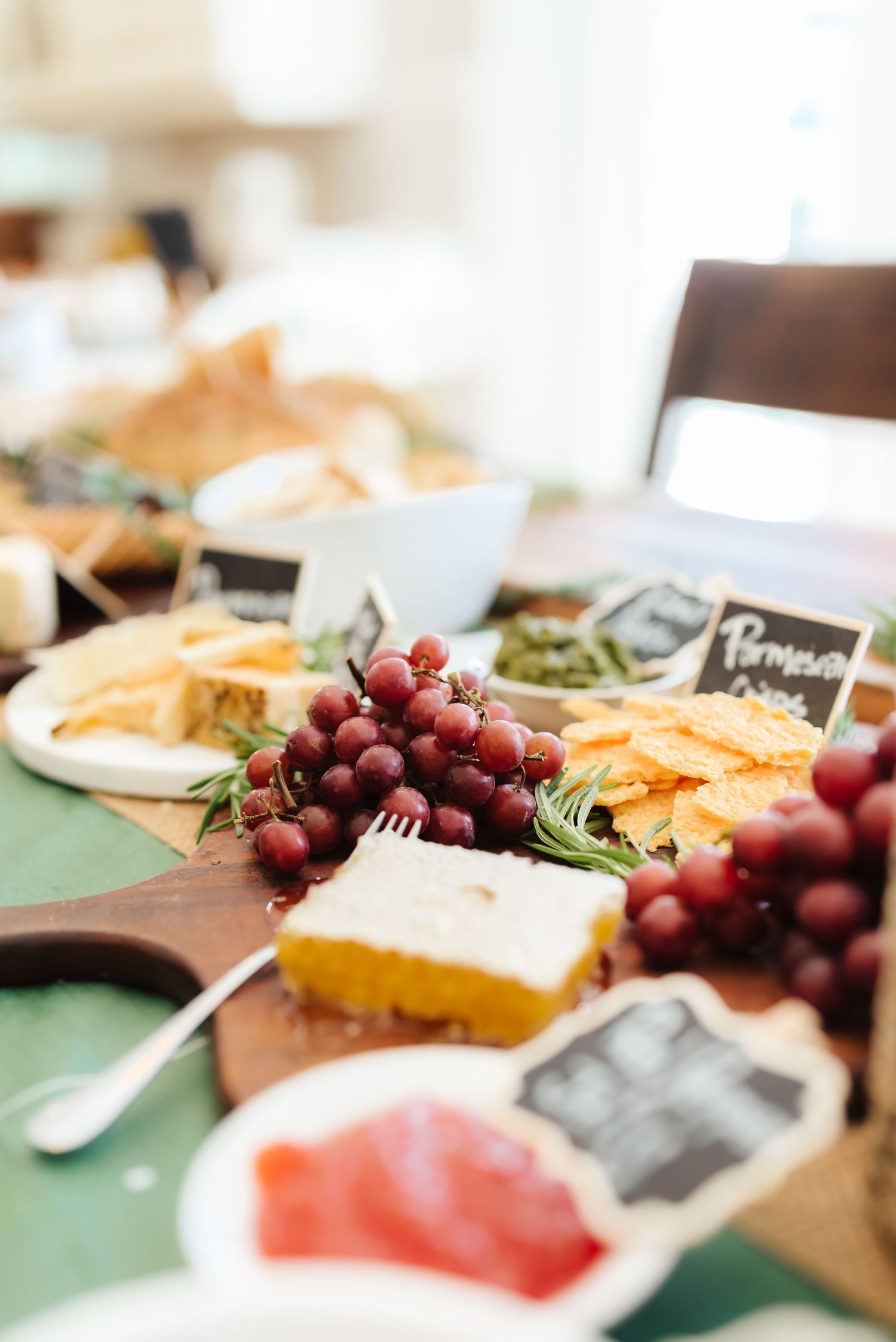 Cheese board spread with red grapes, crackers and various appetizers on a green placemat.